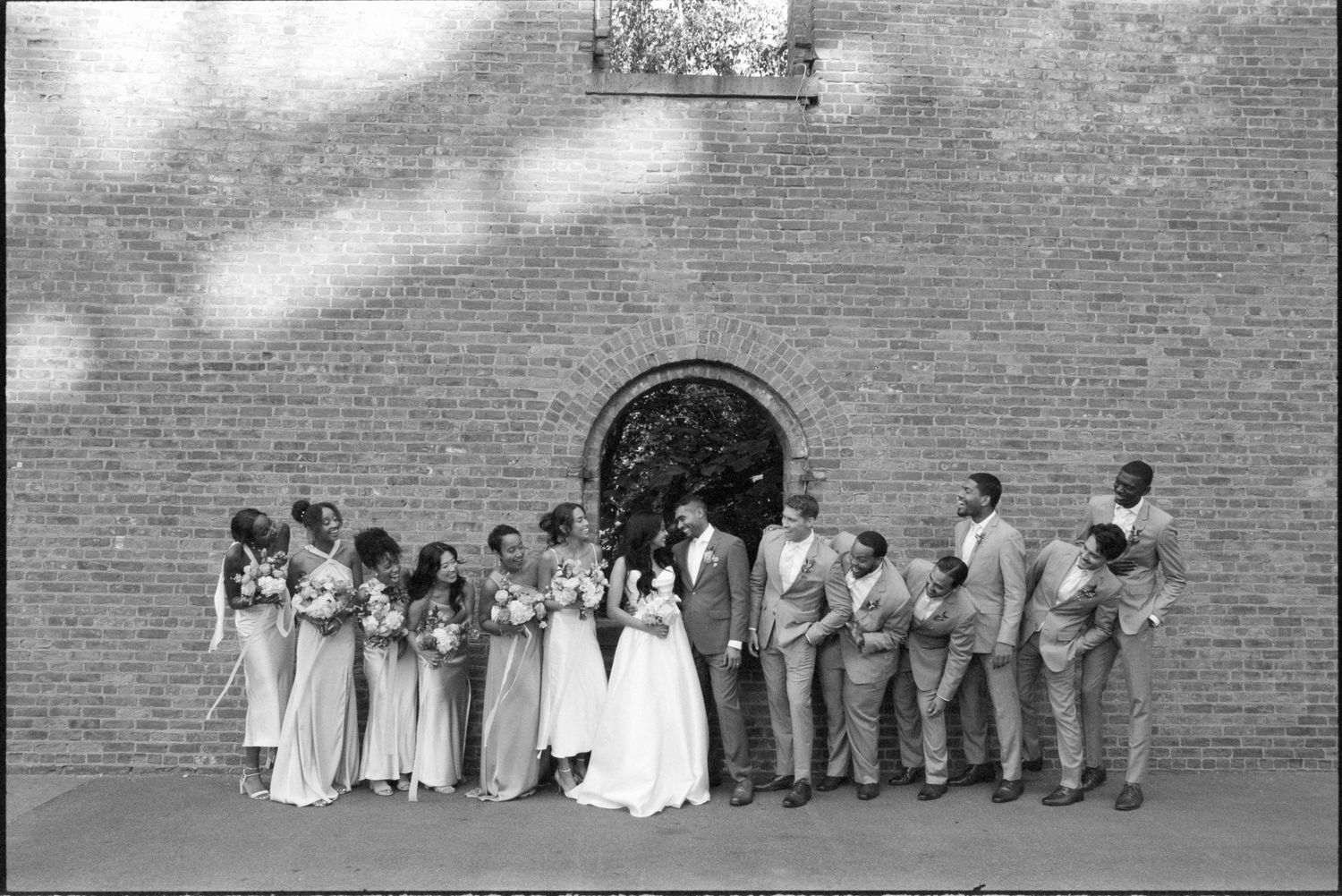A black and white photo showing a group of people lined up against a brick wall.