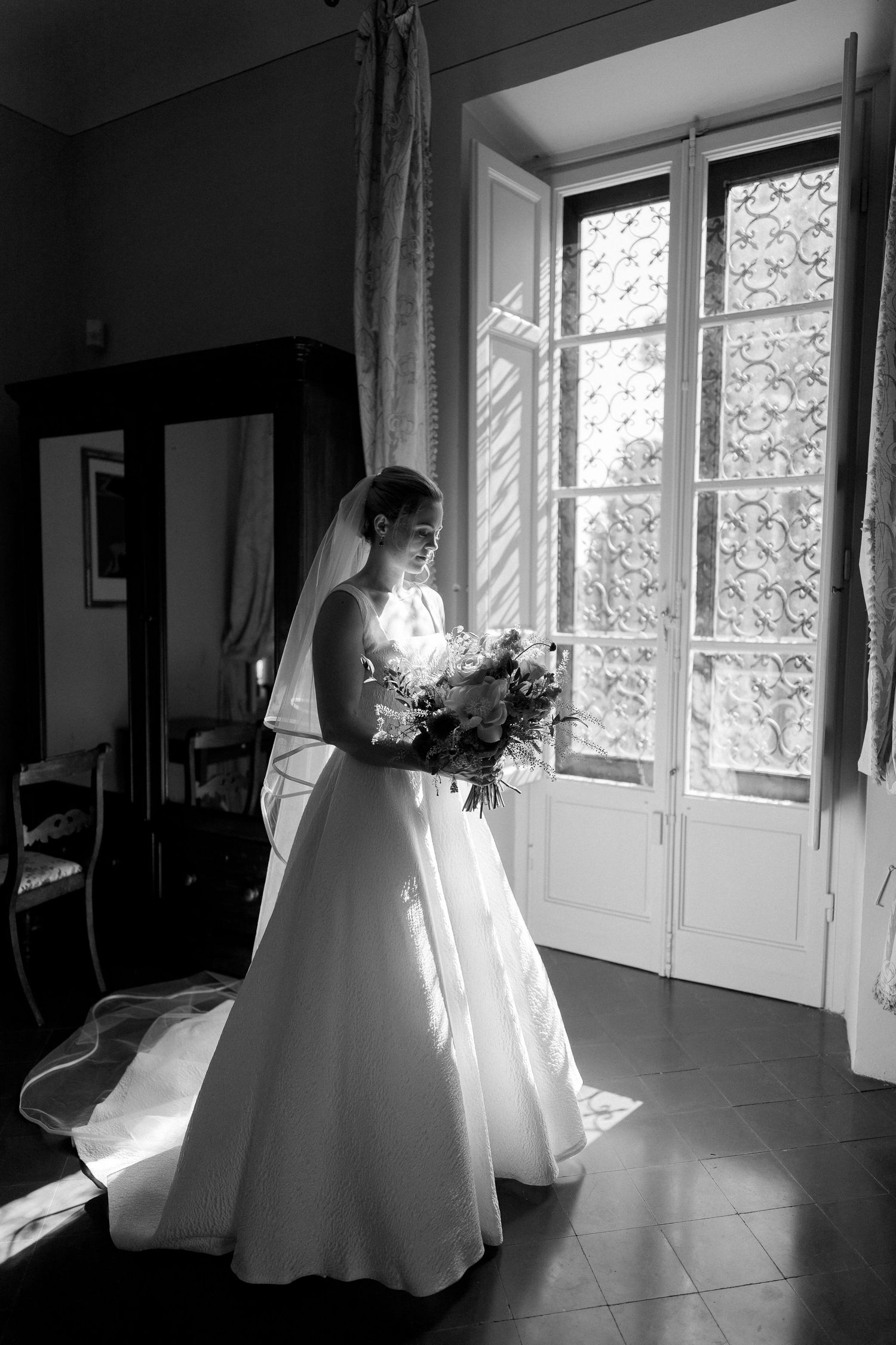 A series of black and white photos showing a bride in a flowing white wedding dress standing near sunlit windows.