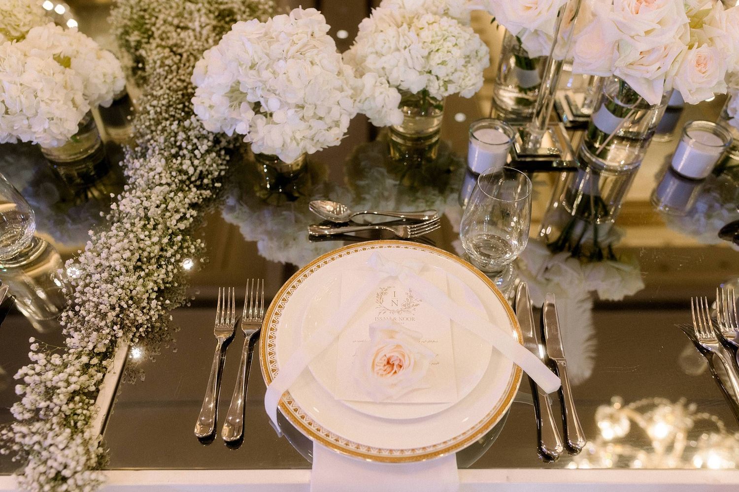 Elegant place setting with gold-rimmed plate and white floral centerpieces on gray tablecloth at wedding reception.