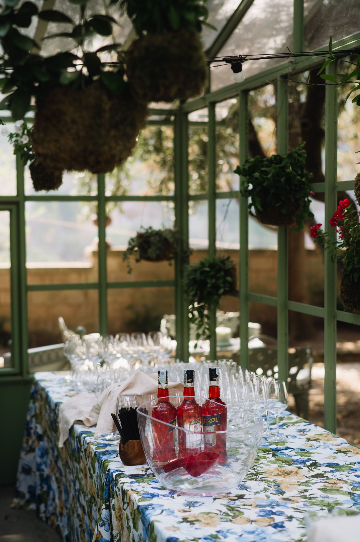 Elegant table settings with wine glasses and colorful floral tablecloths in a greenhouse-style venue for a special event.