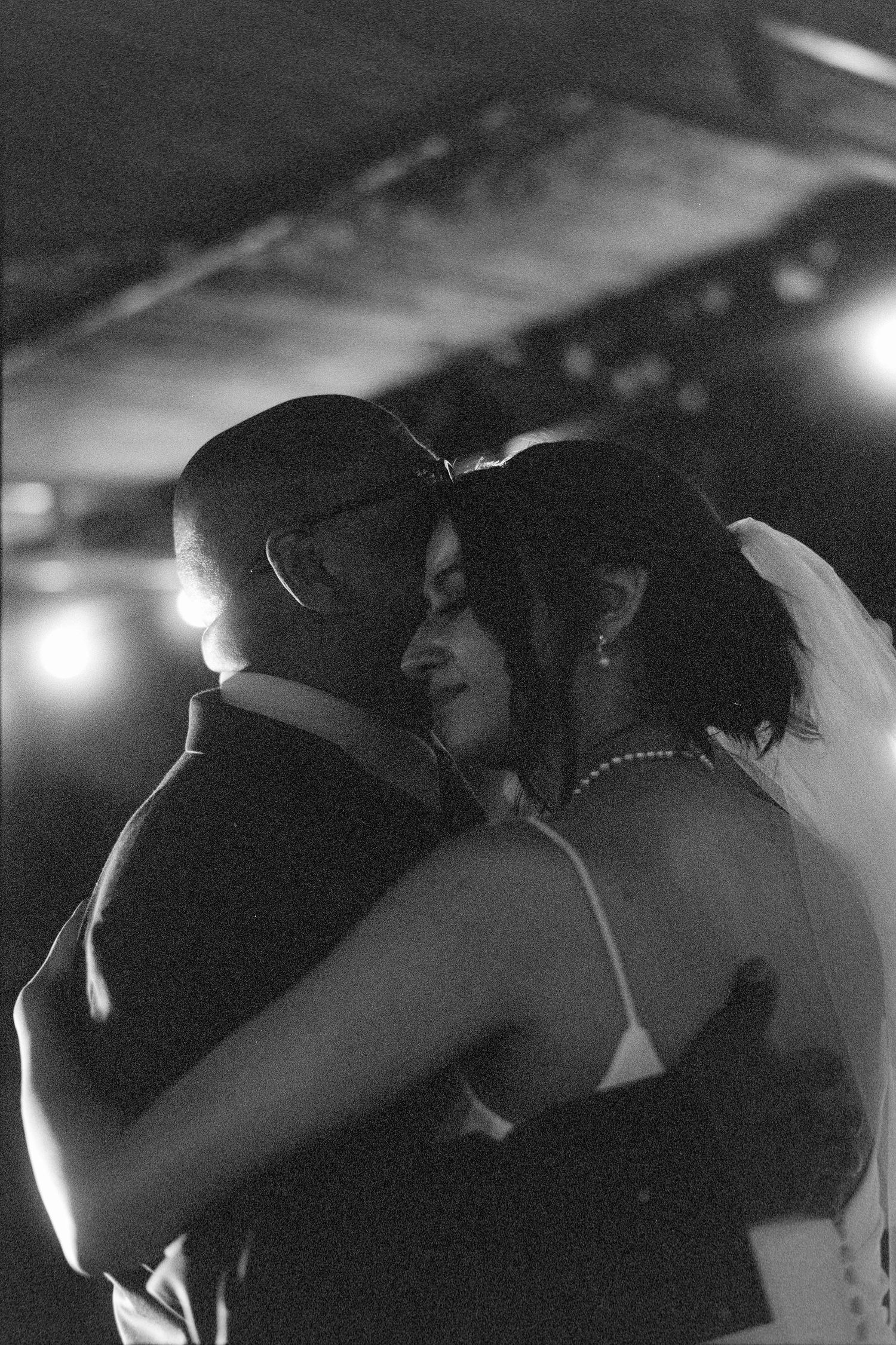 A couple embraces while dancing together in a dimly lit venue with atmospheric lighting.