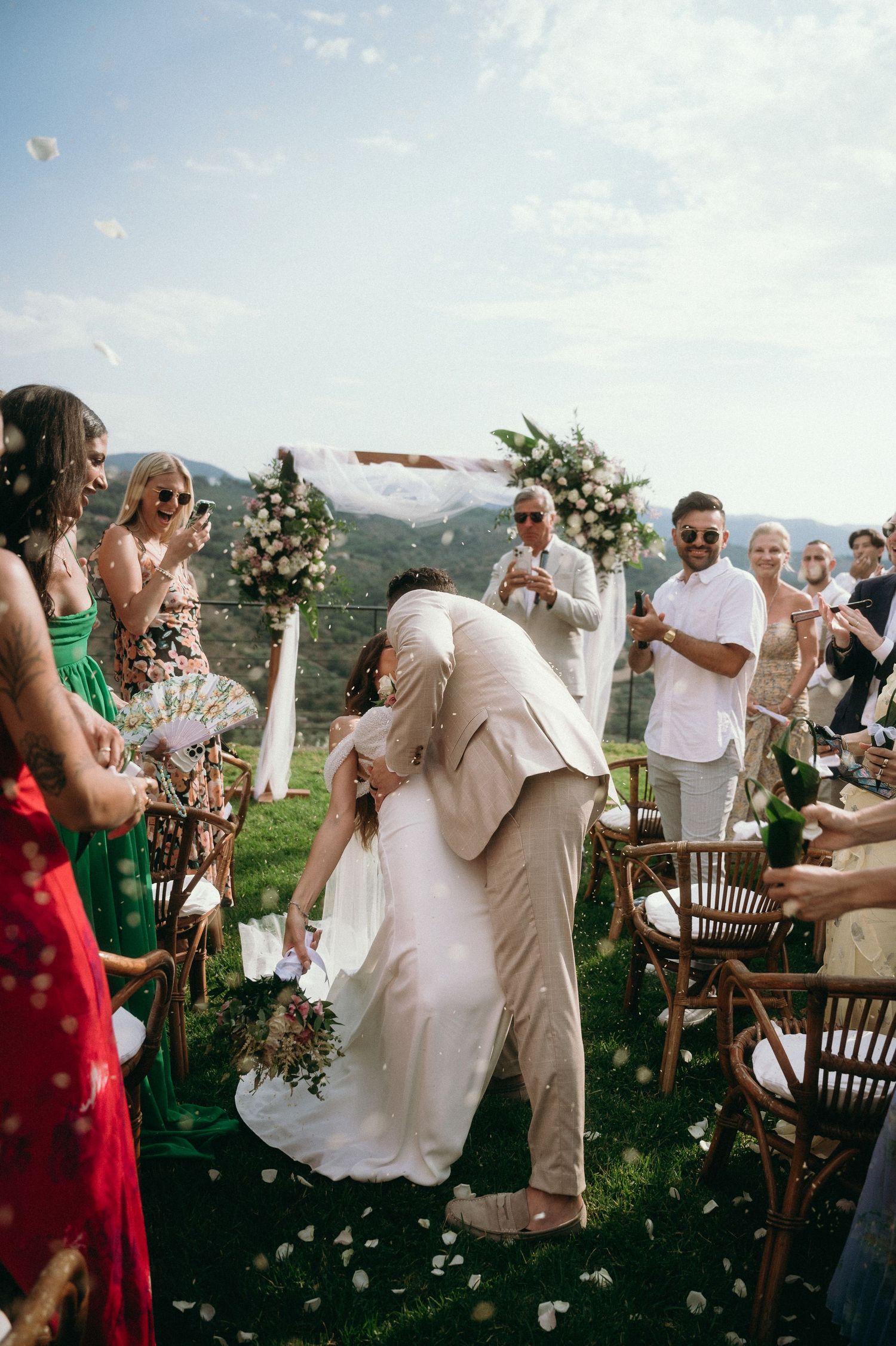 Wedding guests celebrate outdoors with confetti and joyful dancing at a scenic mountain venue during a summer celebration.