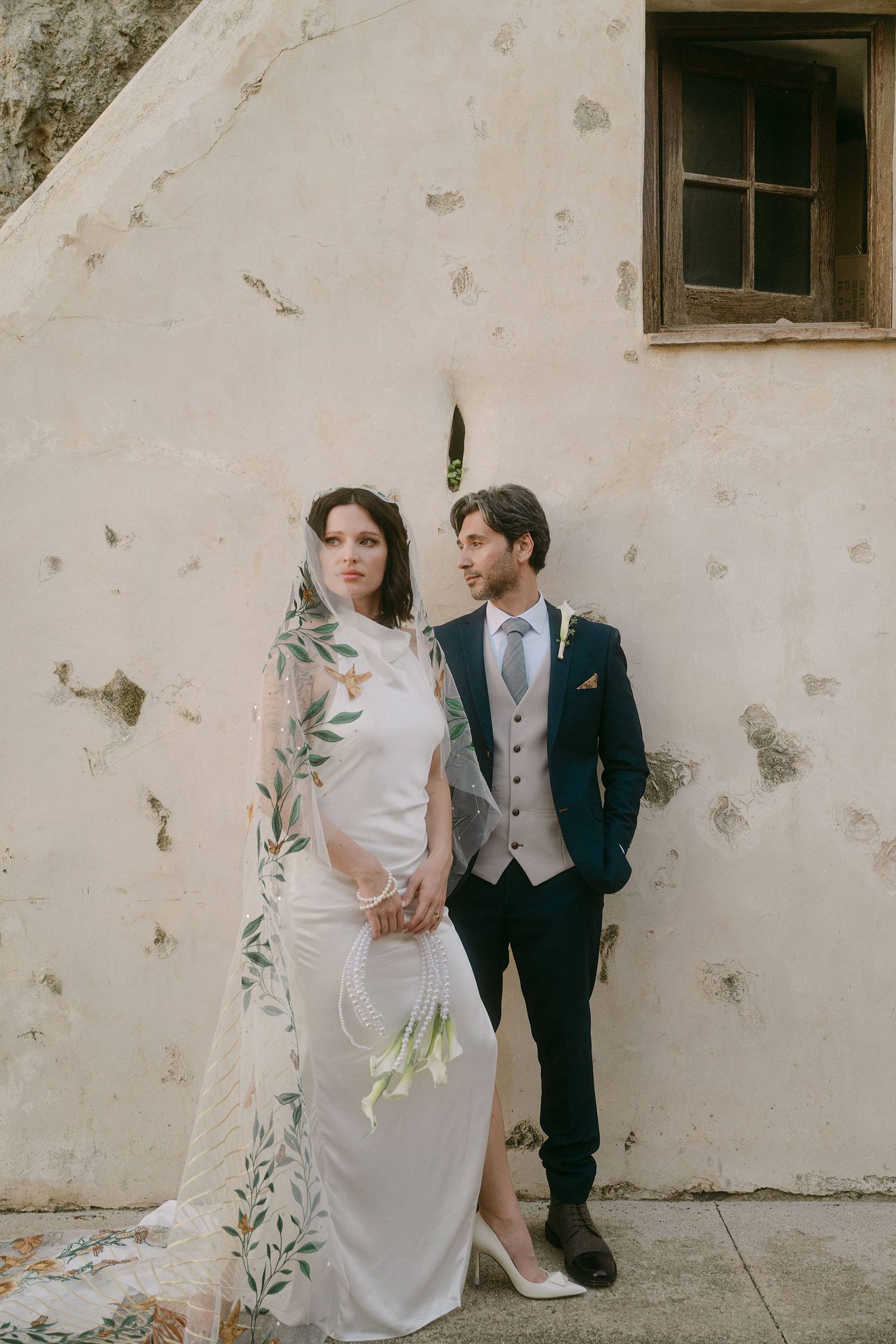 A bride and groom pose against a weathered white wall in a series of artistic wedding photos.