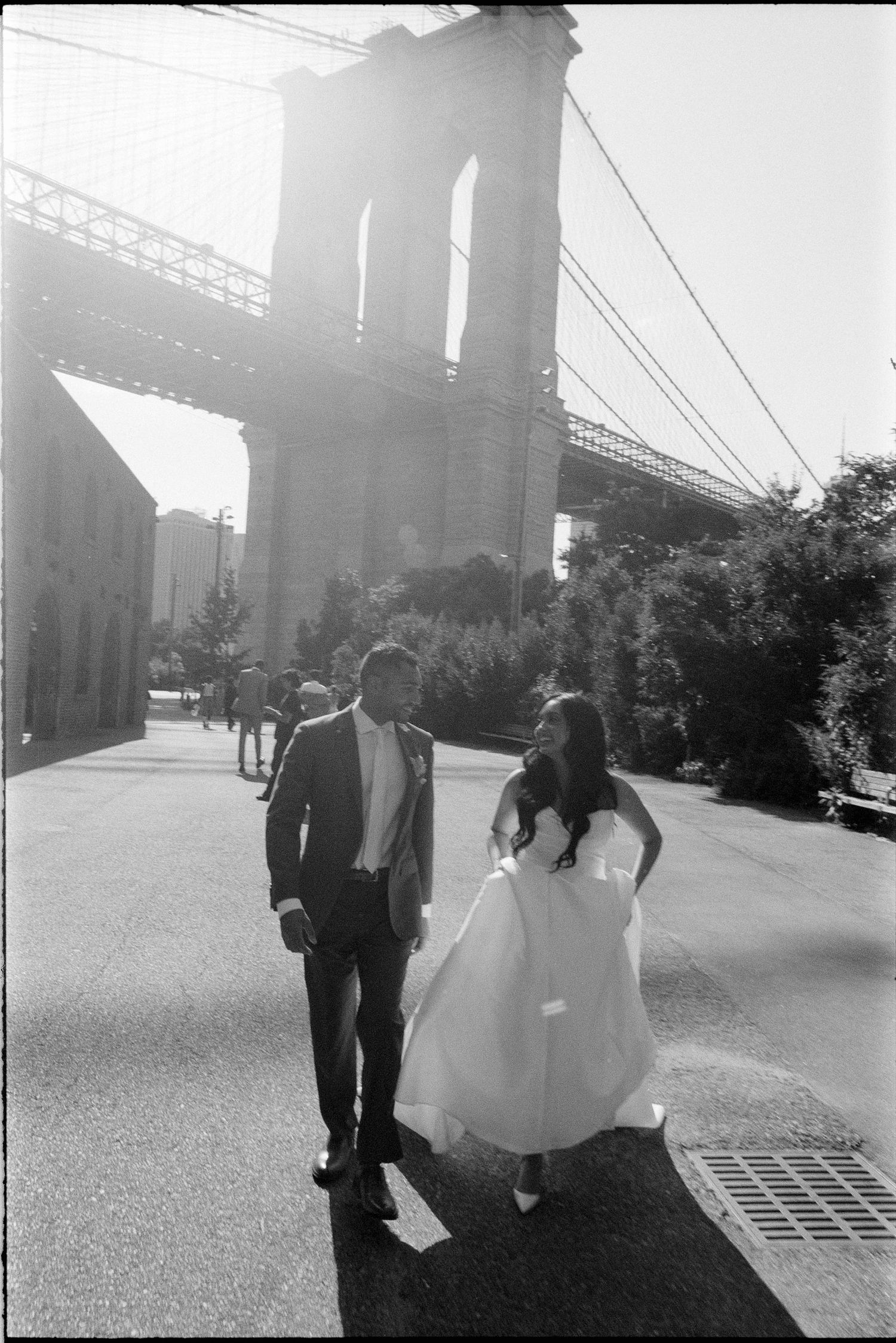 A romantic wedding couple walks together under a bridge in black and white silhouette.