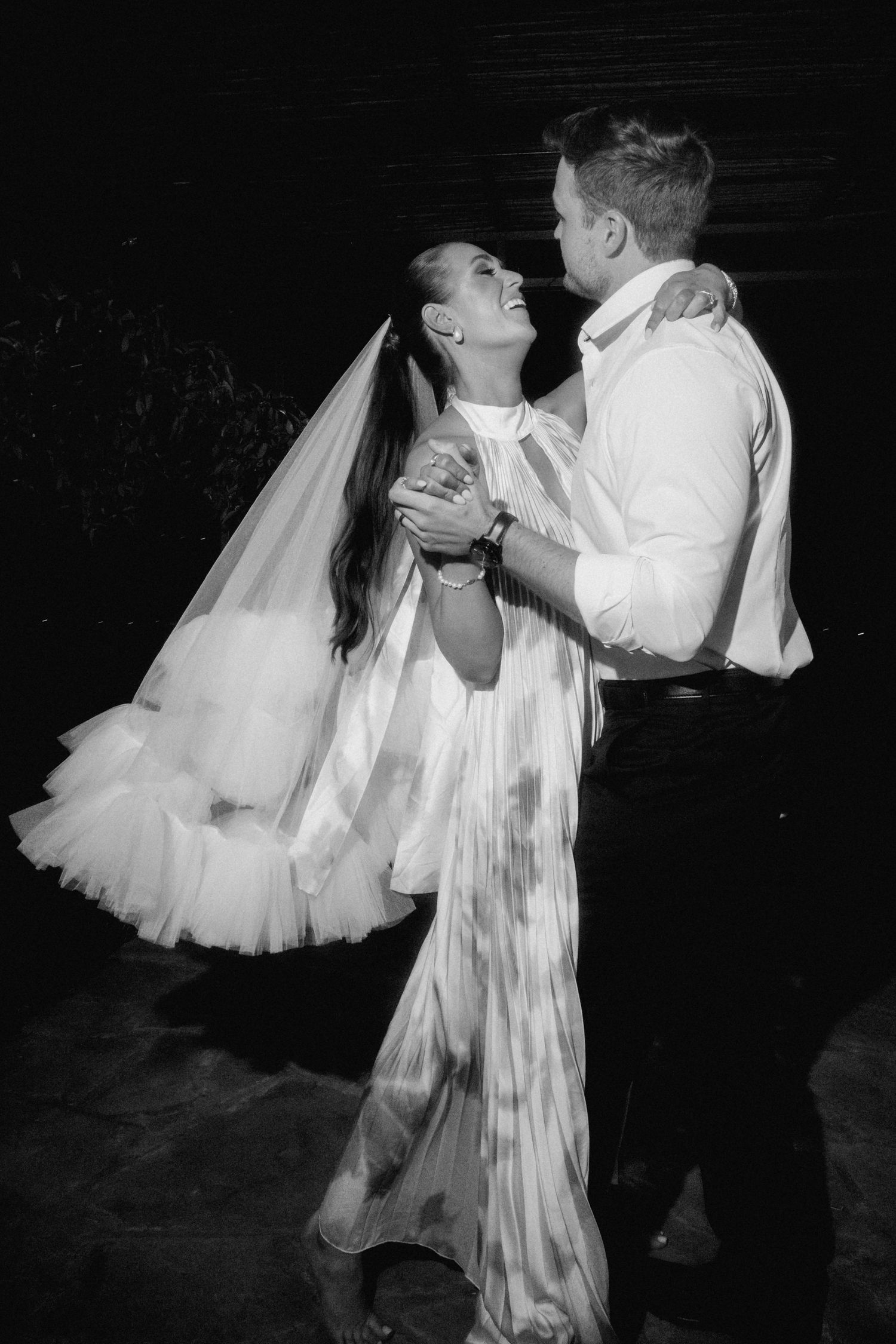 A couple dances together in formal attire, with the bride wearing a flowing white gown and long veil in this vintage photo.