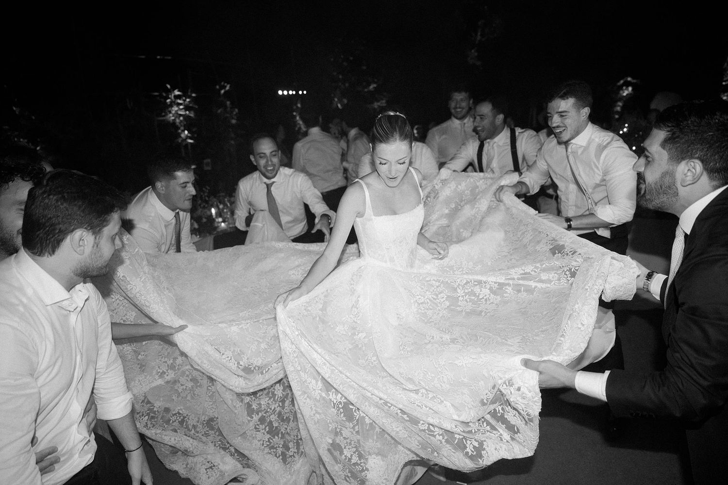 Bride in lace wedding gown dancing joyfully with groomsmen at a lively black and white wedding reception.