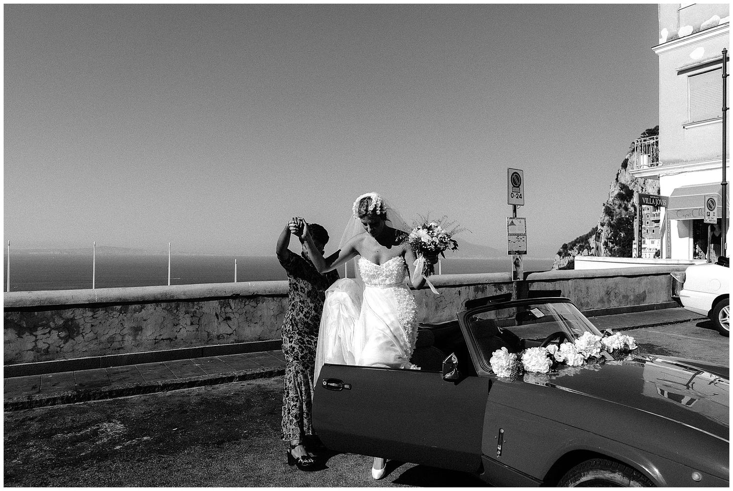 Two people with cameras stand by a car taking photographs near the ocean on a scenic coastal road.