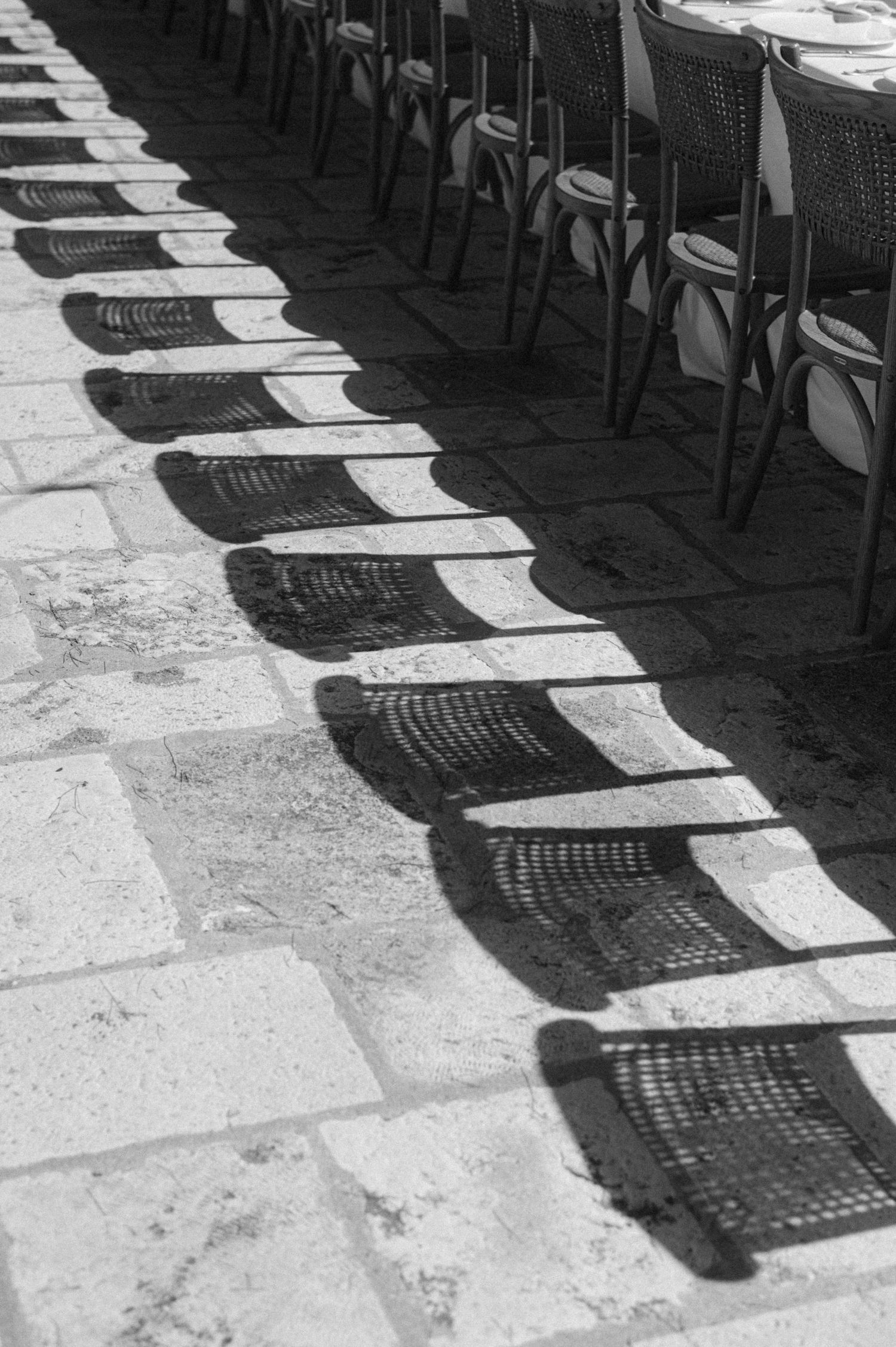 Repeating pattern of chair shadows cast on a stone floor creates a striking black and white geometric design.