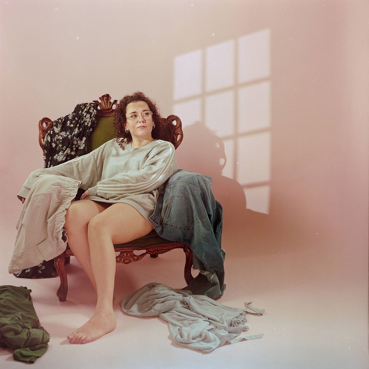 Someone lounges casually in an antique chair with bare feet while sunlight streams through a window onto a pink wall.