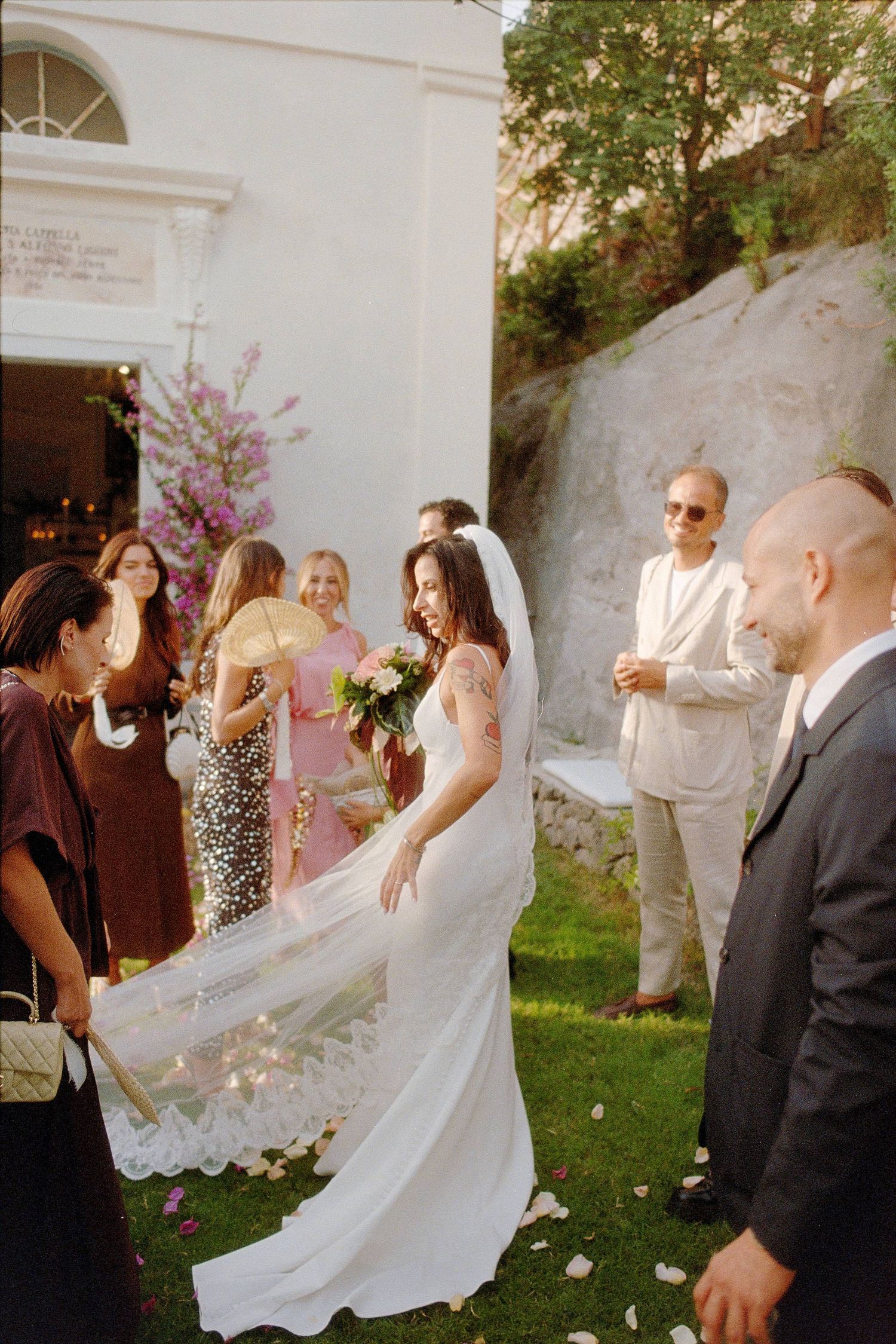 Wedding celebration sequence shows bride's flowing white veil and dress twirling through flower petals in garden setting.