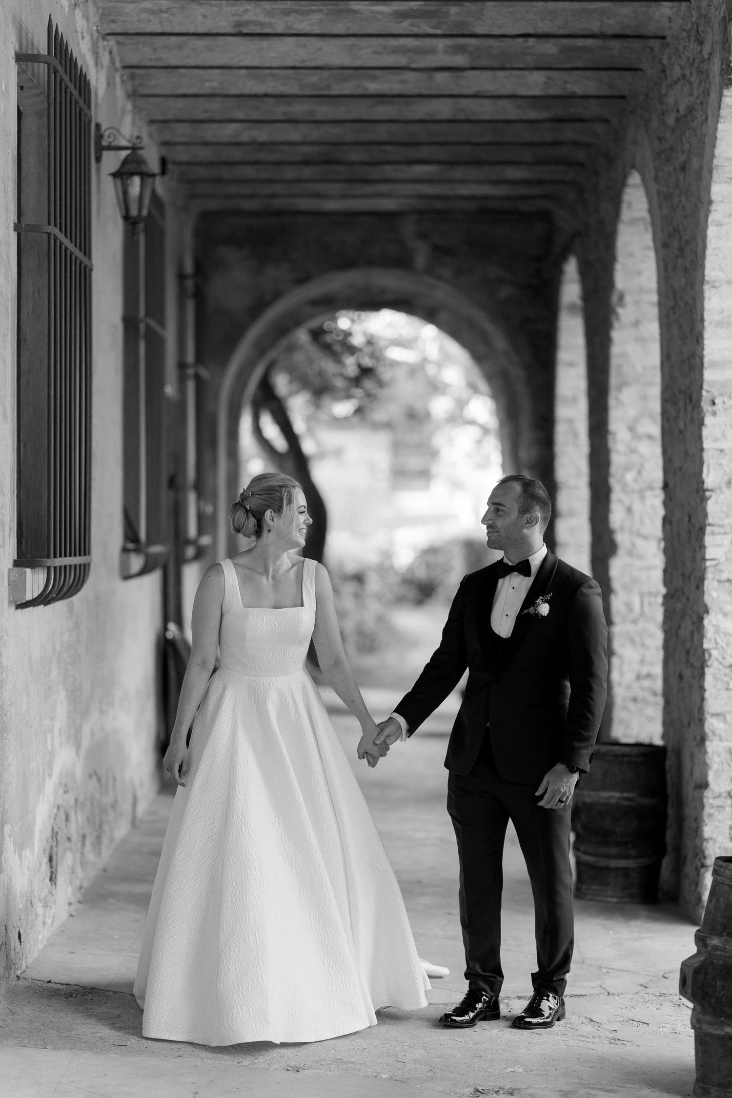 Black and white wedding photo series showing romantic moments between a couple in a stone archway corridor.
