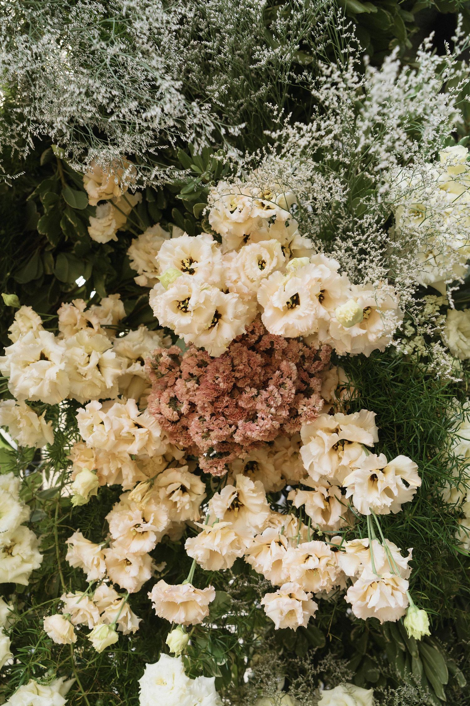 Lush floral arrangement featuring white lisianthus, pink statice, and greenery in an elegant bouquet display.