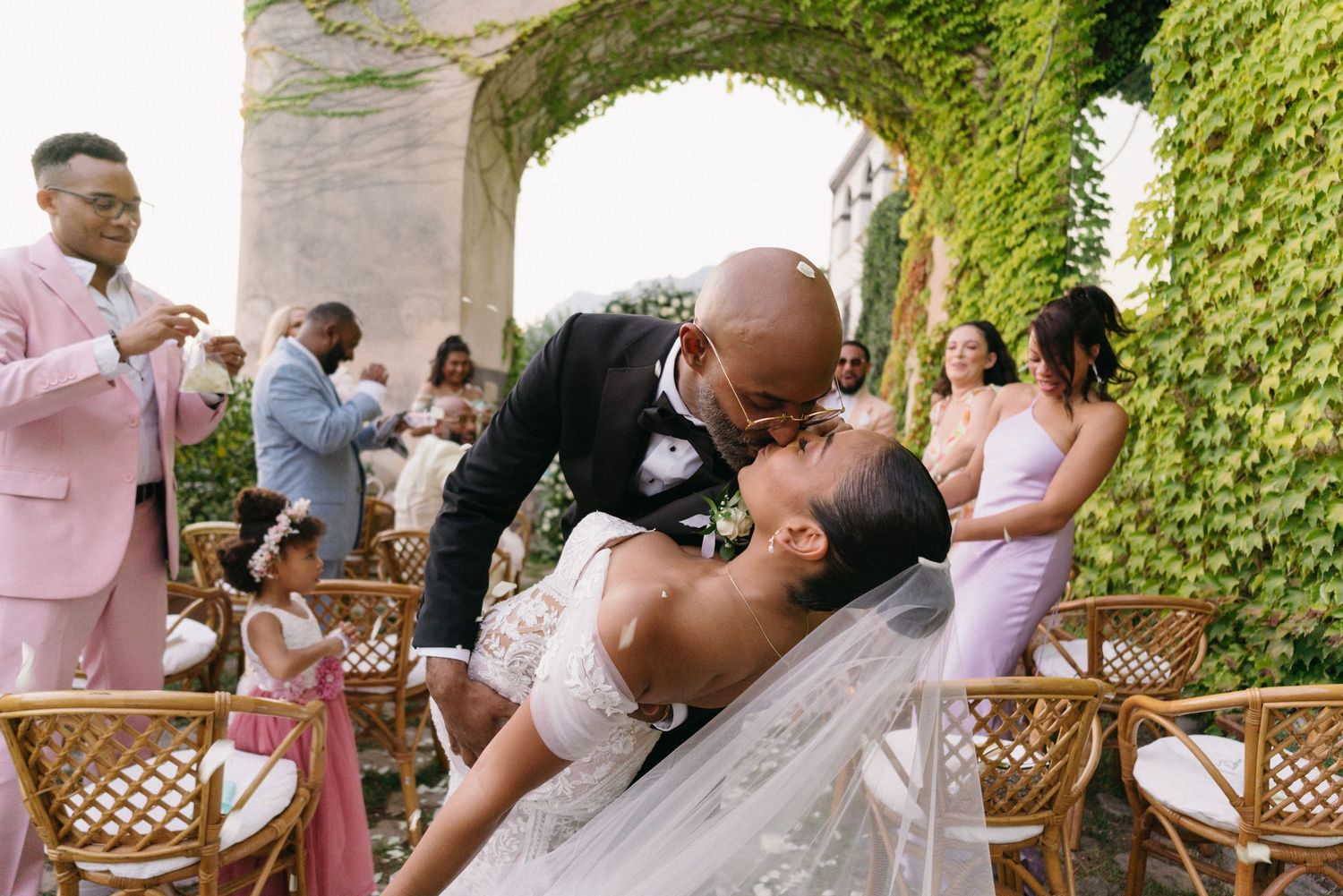 A romantic scene at an outdoor wedding with greenery-covered walls where a couple shares a tender moment.