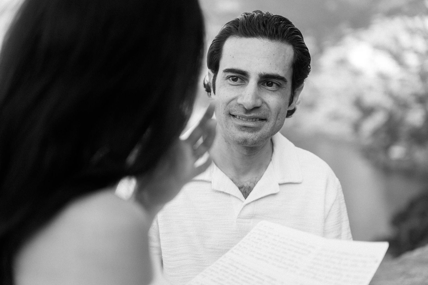 Person in white polo shirt looking attentively at someone reviewing documents in a black and white photo.
