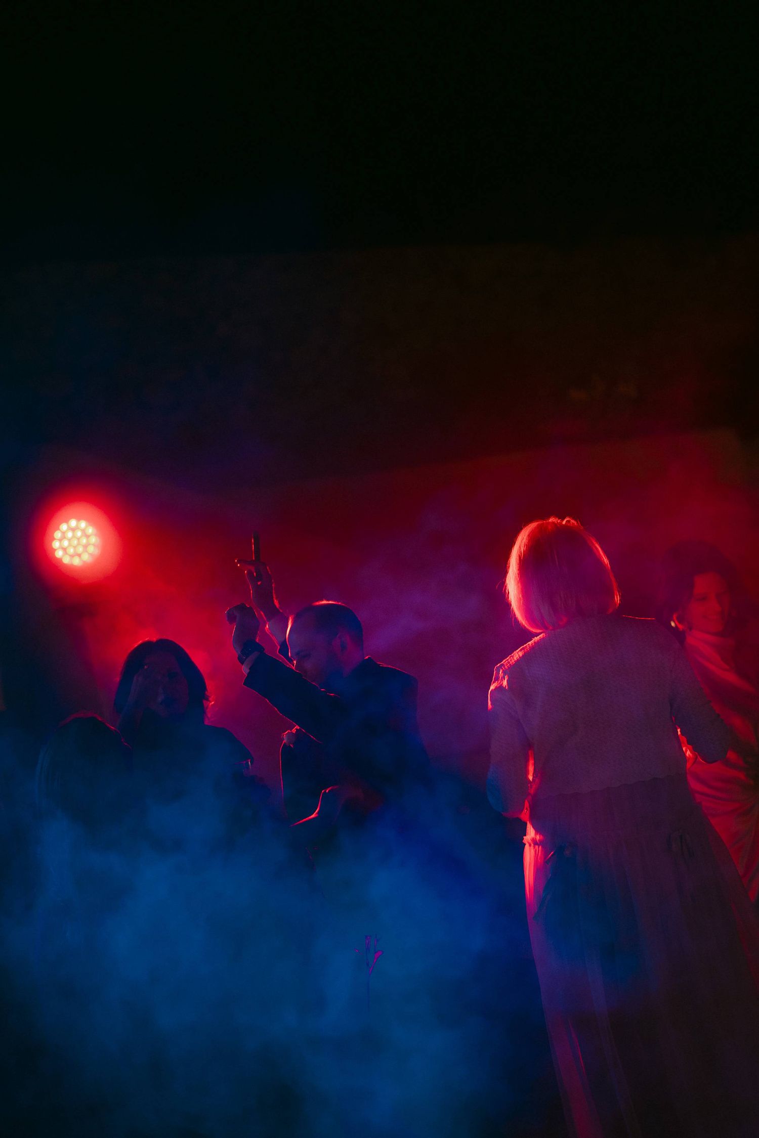 Silhouetted figures dance in a nightclub atmosphere with dramatic red and blue lighting effects creating a moody ambiance.