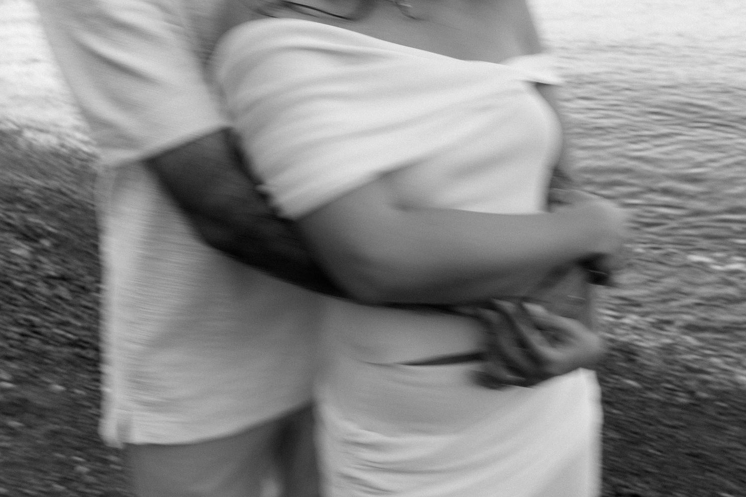 Blurred black and white image showing two people embracing by the water's edge.