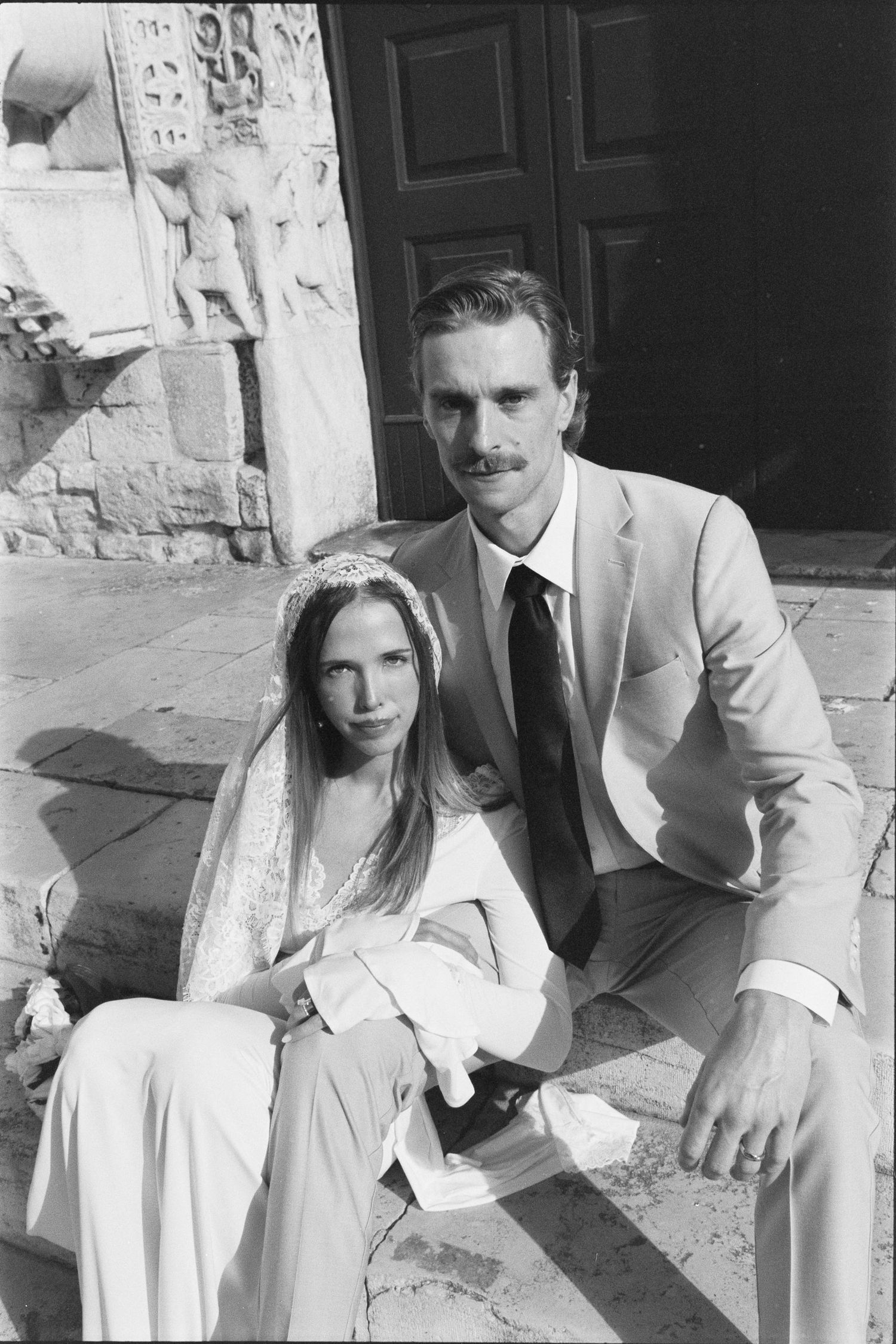 A black and white photo series shows a couple in white outfits sitting together outdoors on stone steps.