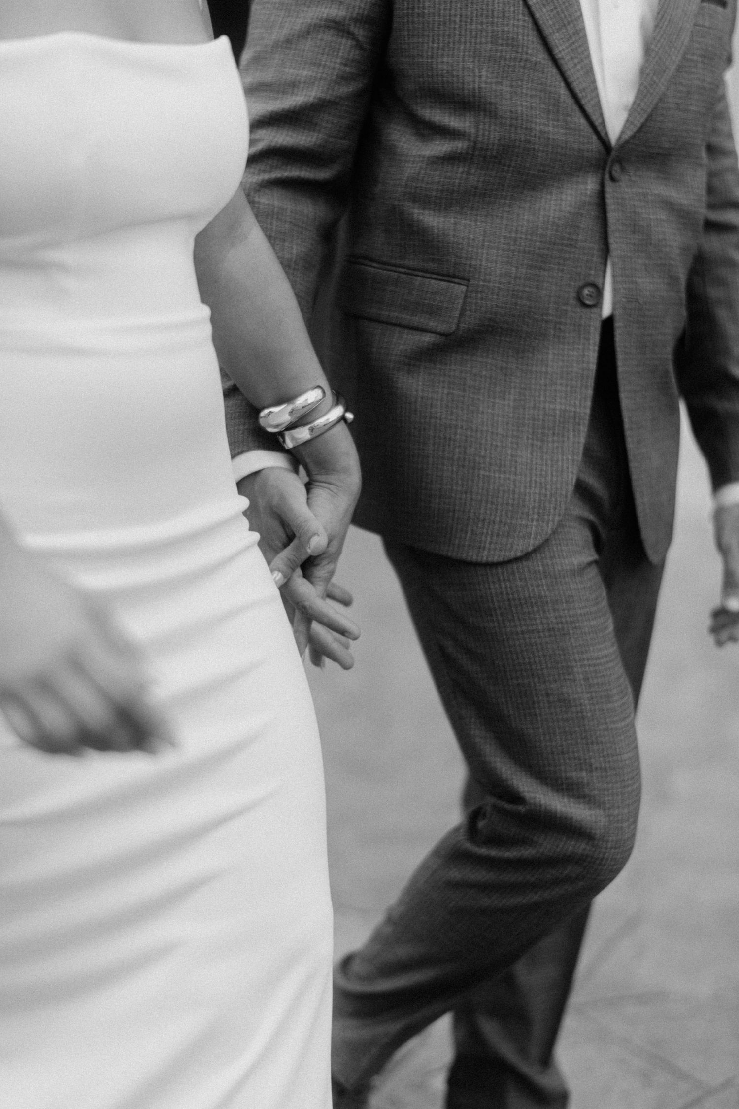 A close-up black and white photo shows a person in a white dress walking next to someone wearing a gray suit.