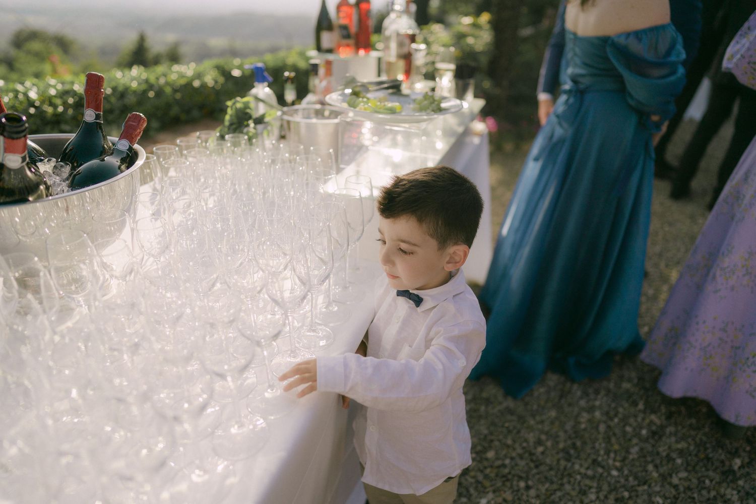 Wedding guests dance and celebrate during an outdoor reception on a gravel path surrounded by greenery.