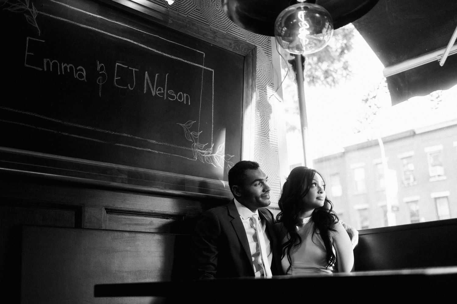 A black and white photograph of a couple sitting together by a window in what appears to be a cafe or restaurant.