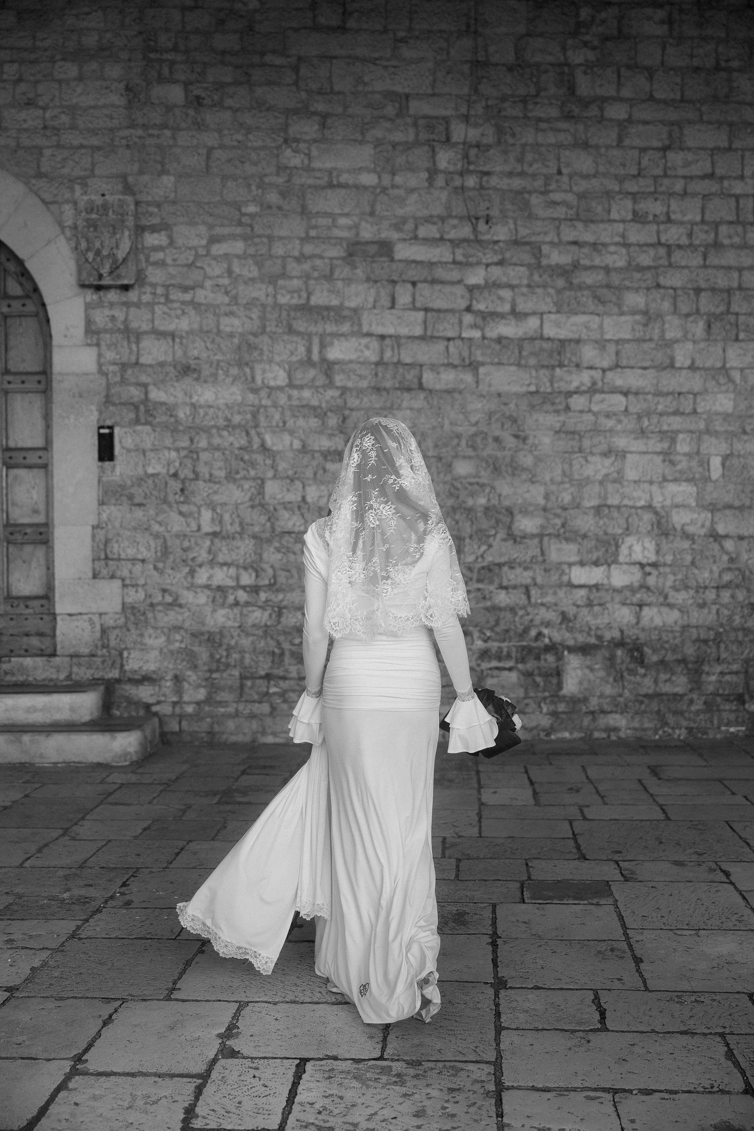 A sequence of black and white photos showing a figure in white dress moving across a stone floor against a brick wall.
