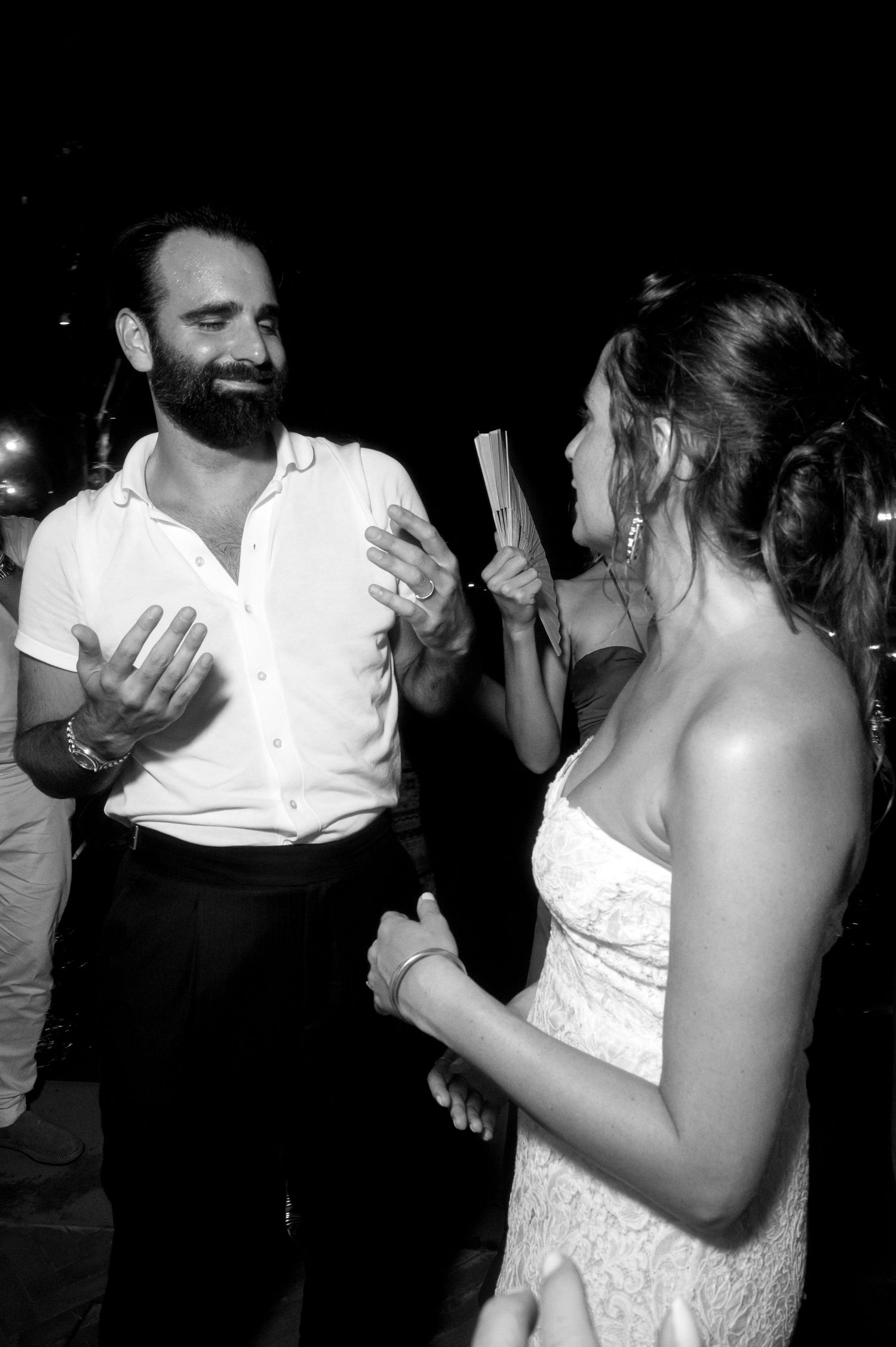 A candid black and white photo of two people dancing at a wedding reception, with one in a white dress.