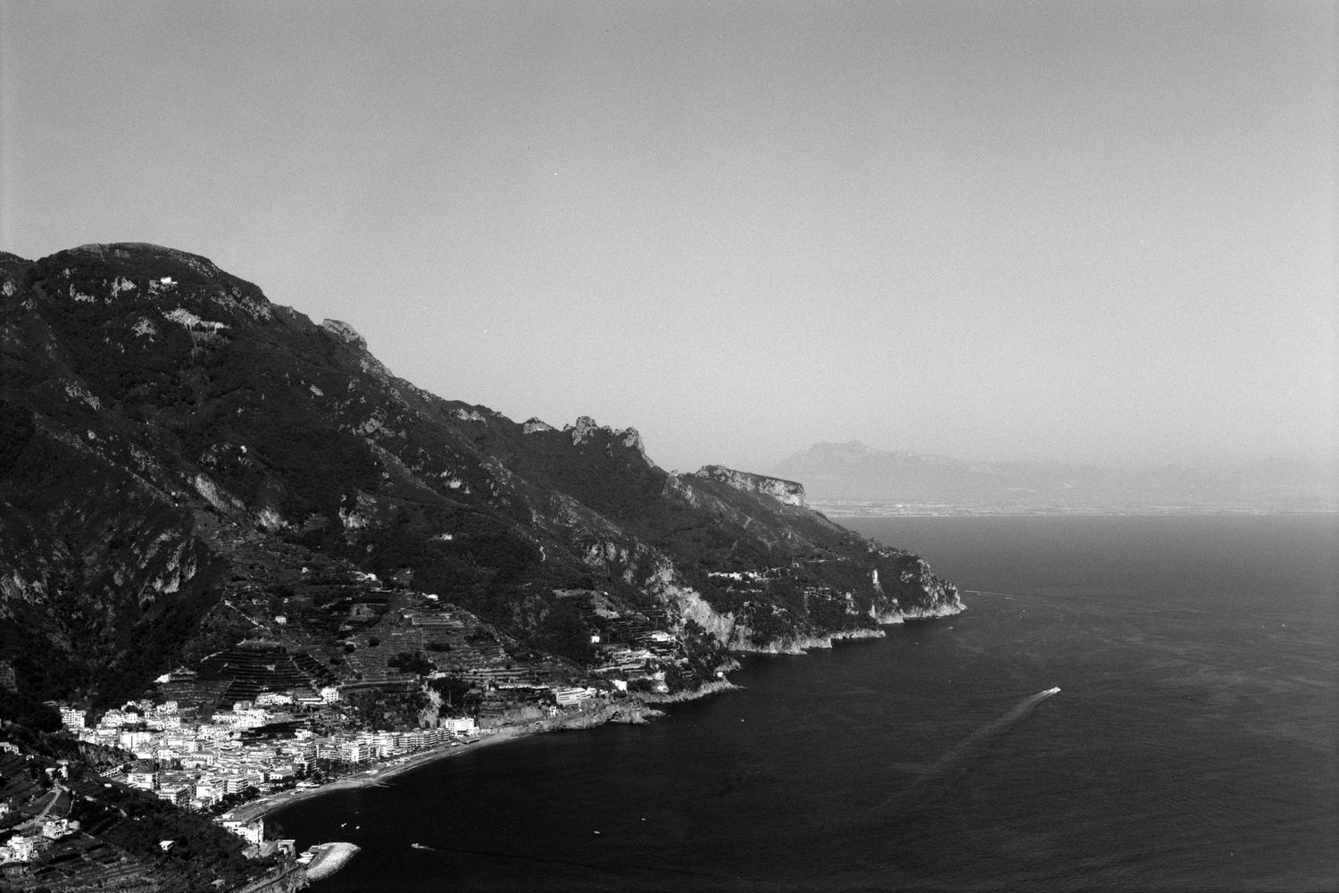Black and white aerial view of a coastal town nestled along mountain cliffs overlooking the Mediterranean Sea.