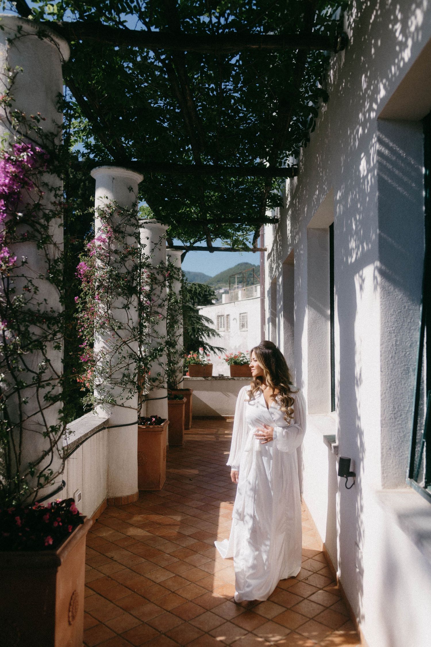 A sunlit Mediterranean style porch walkway with white columns and terracotta tiles creates a serene architectural scene.