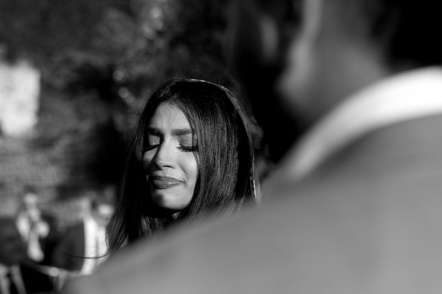 Black and white candid photograph showing a woman with long dark hair smiling with her eyes closed.