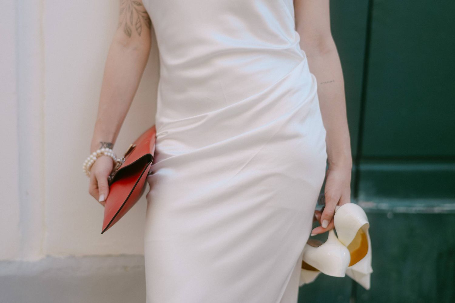 A close-up detail of a sleek white wedding dress with a red clutch visible.