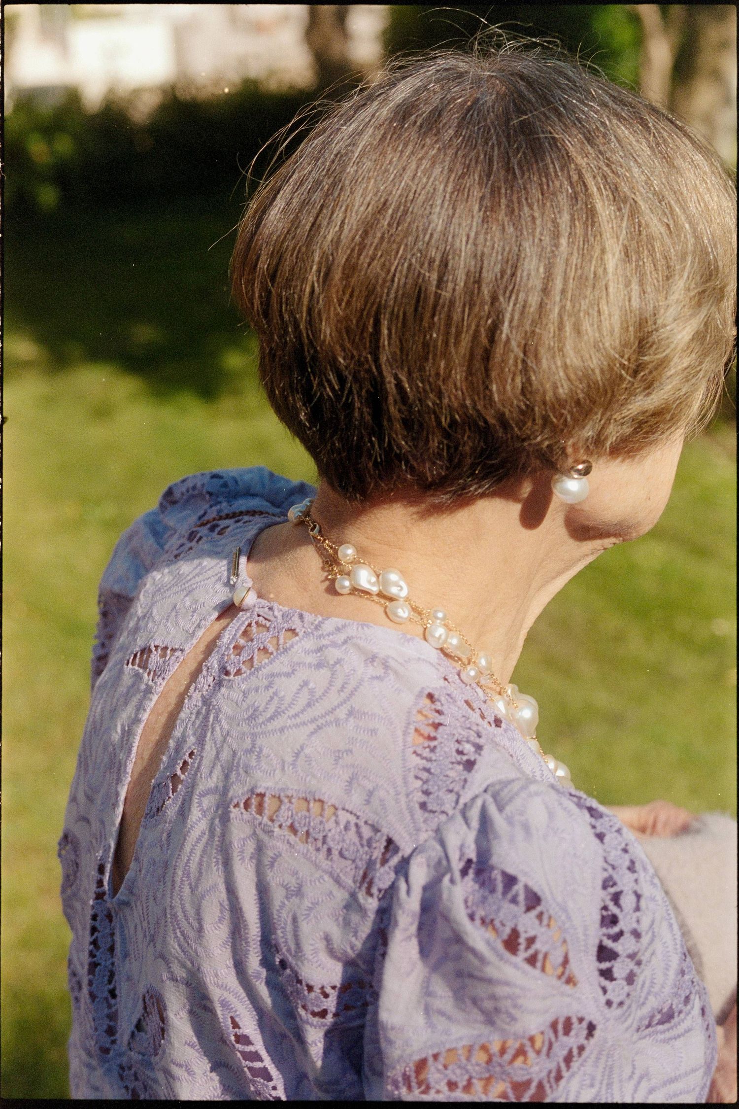 Back view of someone wearing a delicate lavender lace dress with a pearl necklace outdoors in sunny weather.