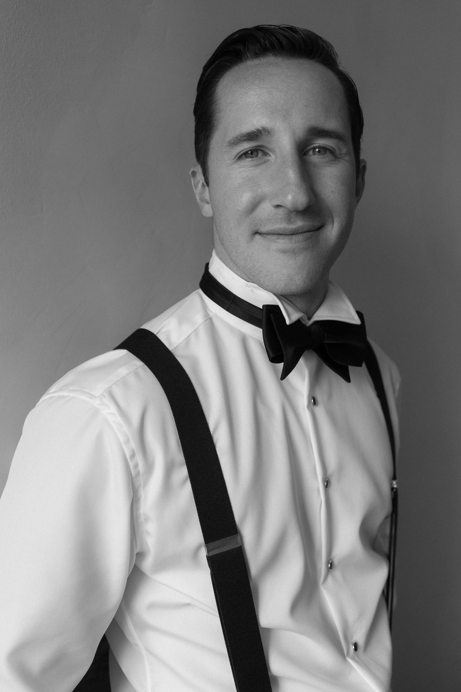 A black and white photo series showing someone adjusting their bowtie and suspenders while wearing a white dress shirt.