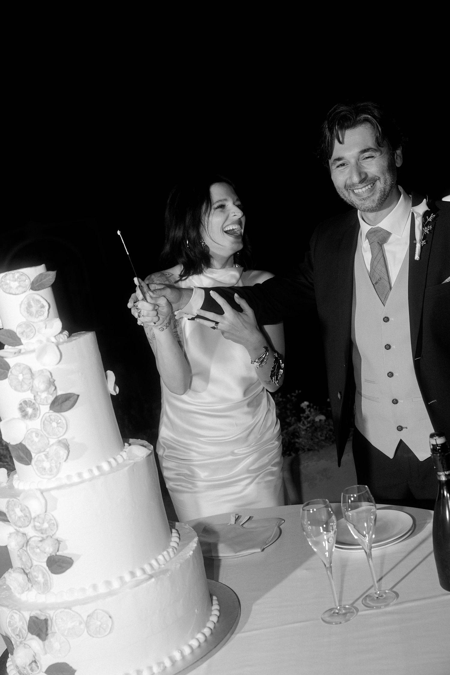 A sequence of black and white wedding photos showing a couple at their reception table with a tiered white wedding cake.