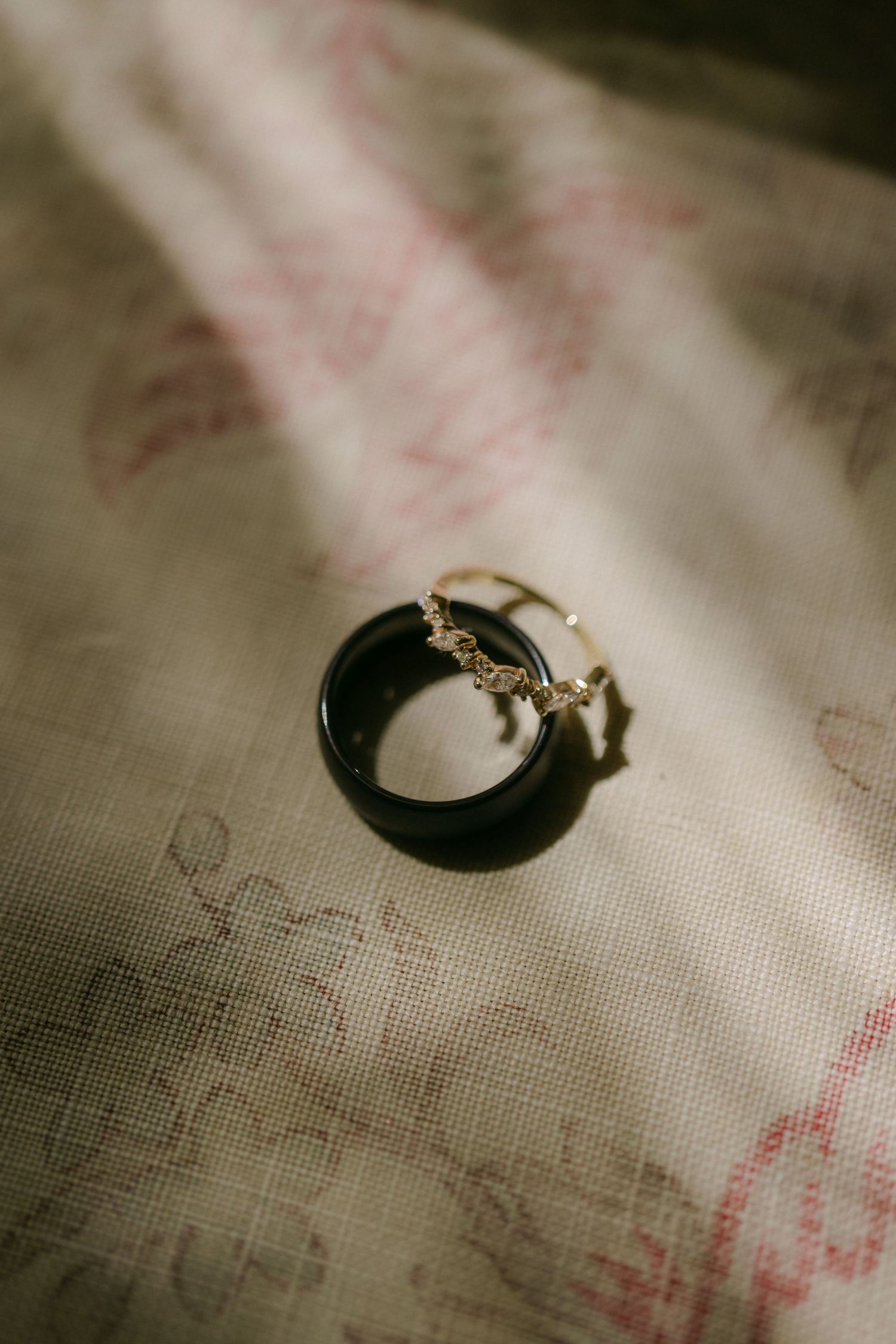 A black ceramic or resin ring with gold butterfly accents sits on a textured fabric with soft lighting.