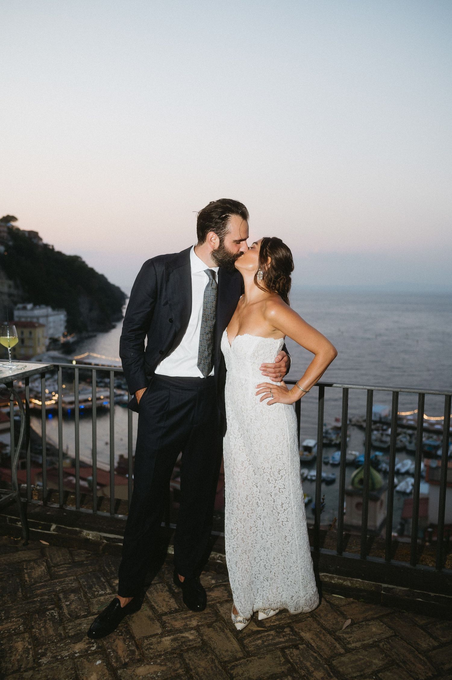 Romantic wedding couple sharing intimate moments on a scenic coastal balcony overlooking the ocean at sunset.