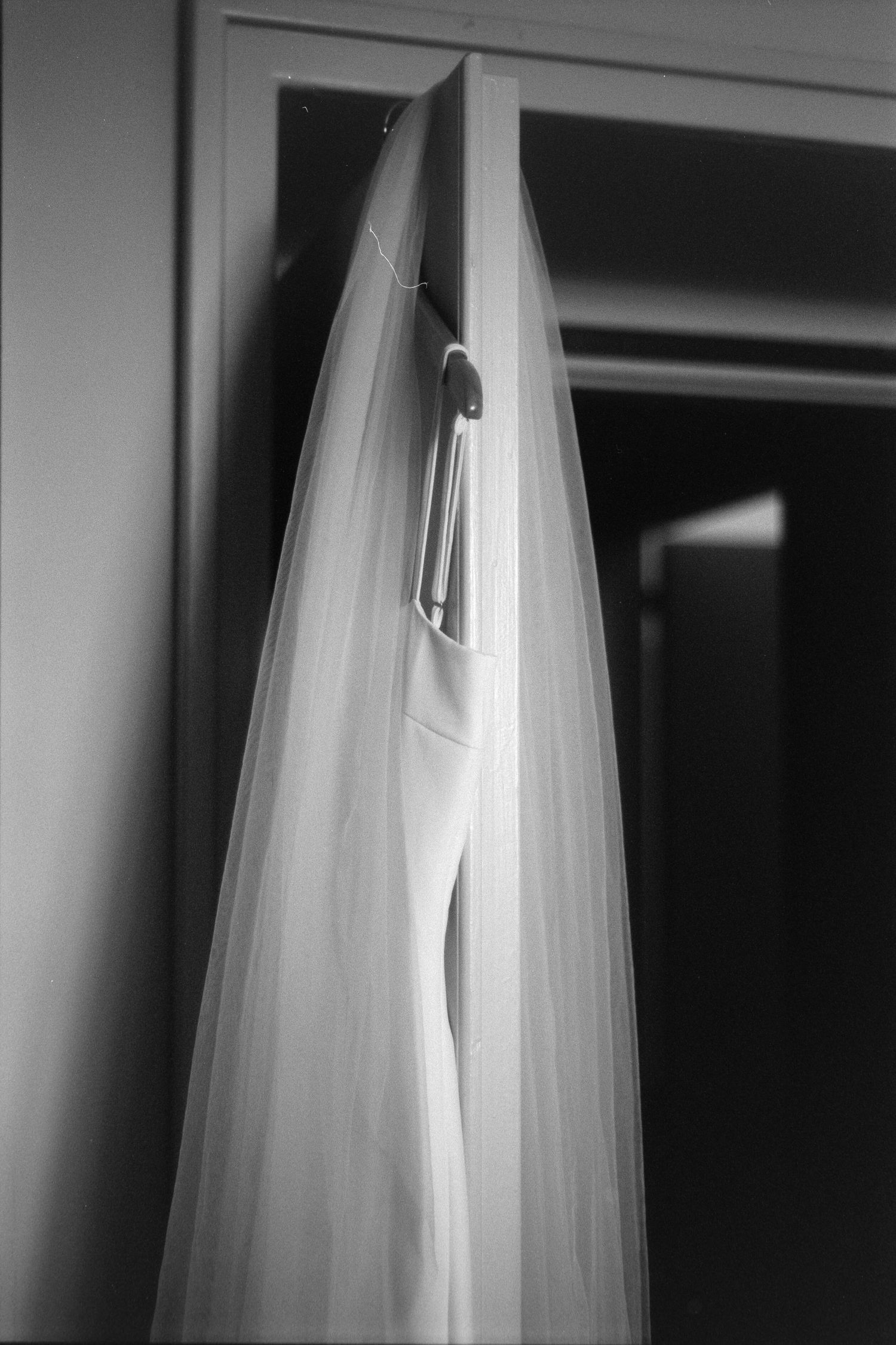 A delicate white wedding veil hangs elegantly from a hanger in a black and white photograph.