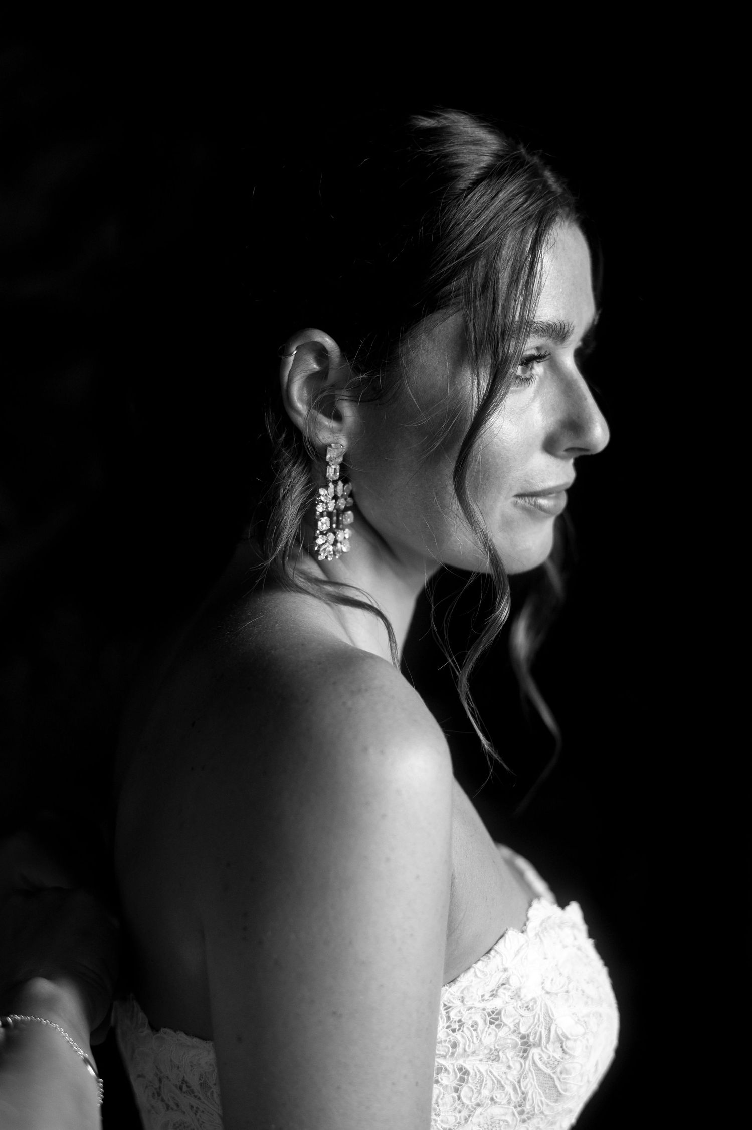 Dramatic black and white profile portrait of a bride wearing a lace strapless dress and dangling earrings.