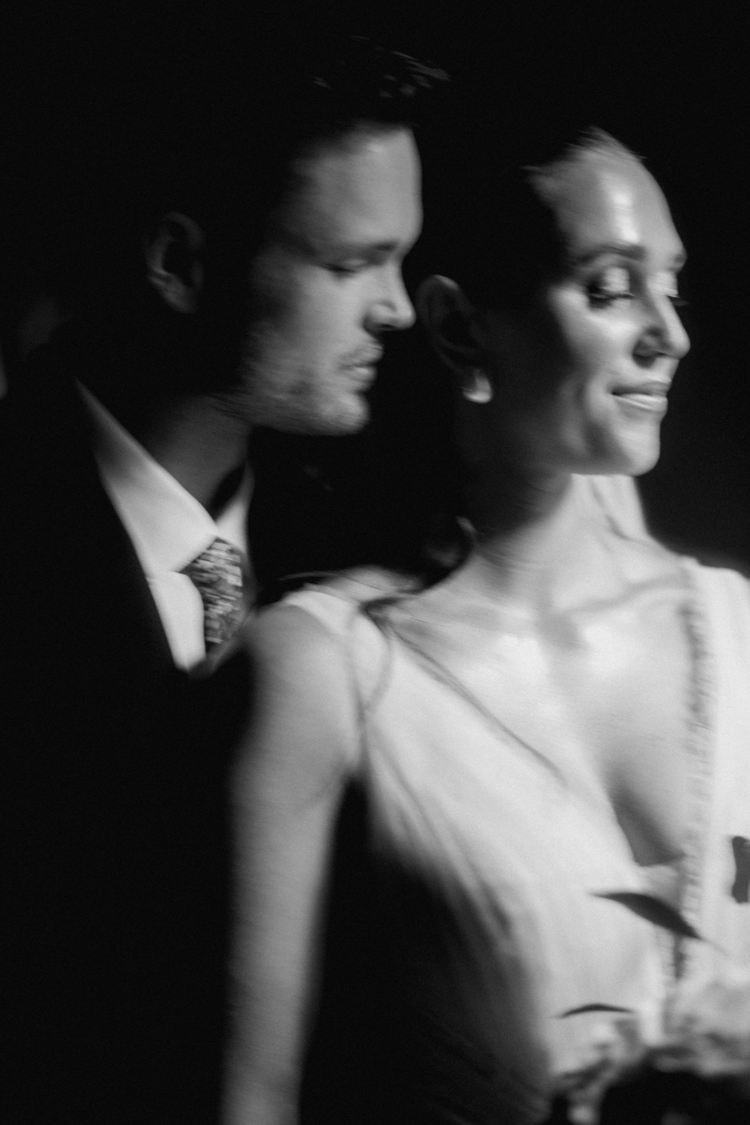 An artistic black and white close-up portrait of a couple in formal wedding attire with soft, dreamy lighting.