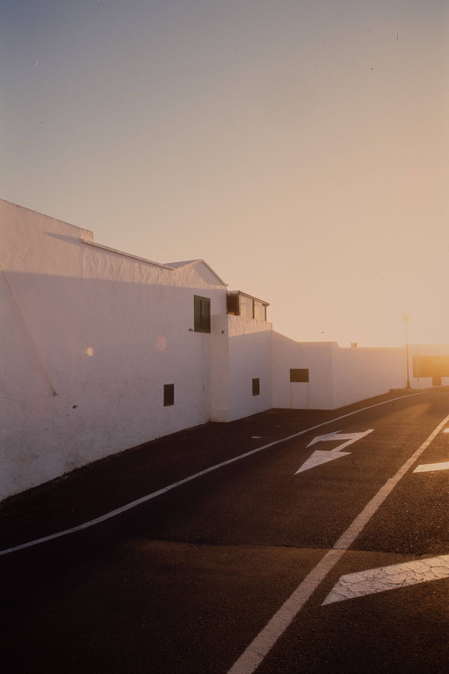 White Mediterranean building along an empty street at sunset with dramatic golden light and road markings on asphalt.