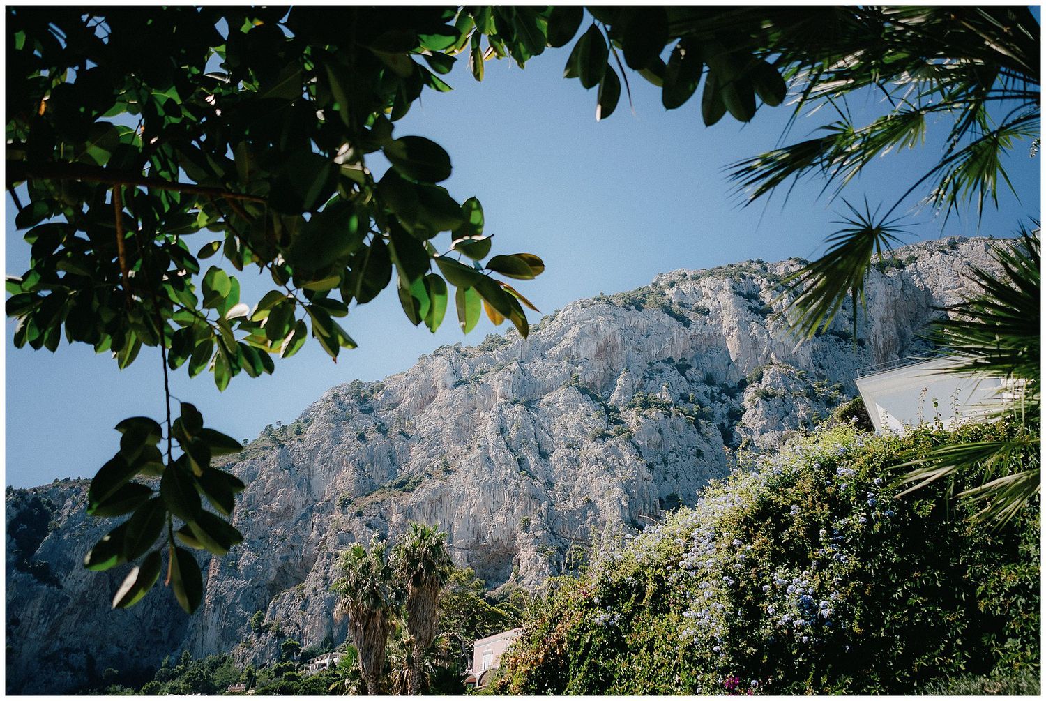 Mediterranean mountainous coastline with lush greenery and dramatic rocky cliffs against blue sky.
