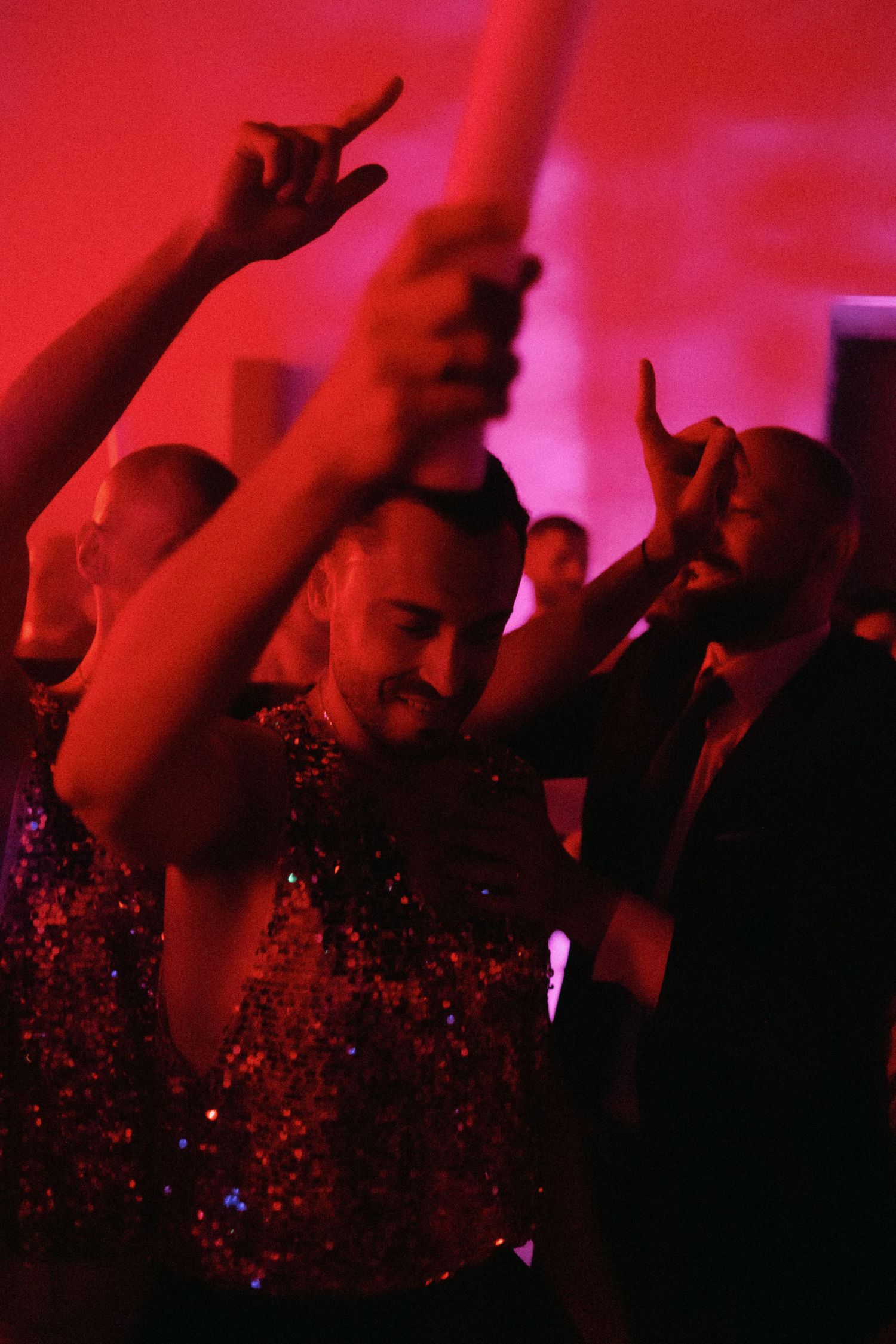 Silhouetted crowd with raised hands at a concert venue illuminated by dramatic red lighting.