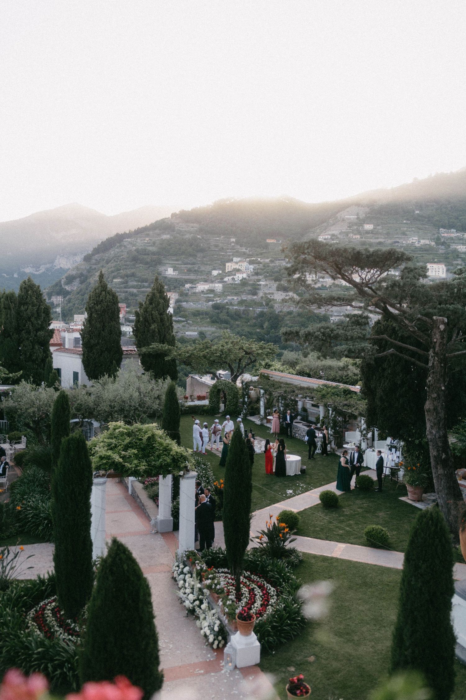 Elegant outdoor wedding ceremony in a Mediterranean garden with cypress trees and mountain views at sunset.