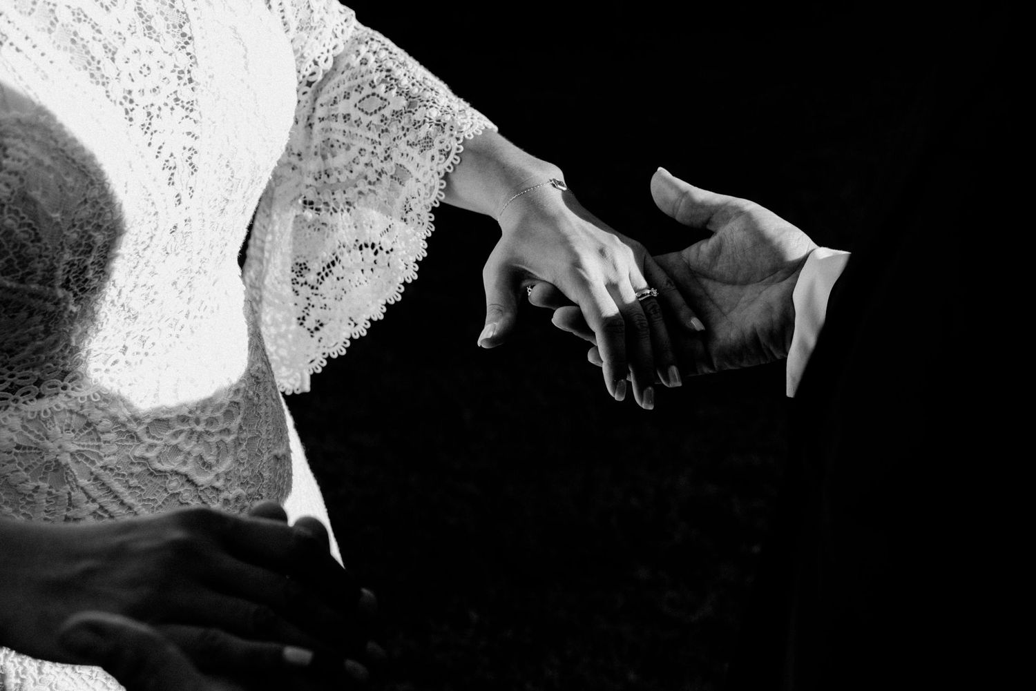 Black and white close-up photograph of two hands reaching toward each other against a dark background.