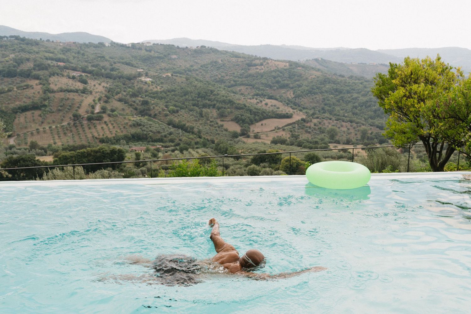 Person swimming in an infinity pool overlooking scenic mountain landscapes and valleys.