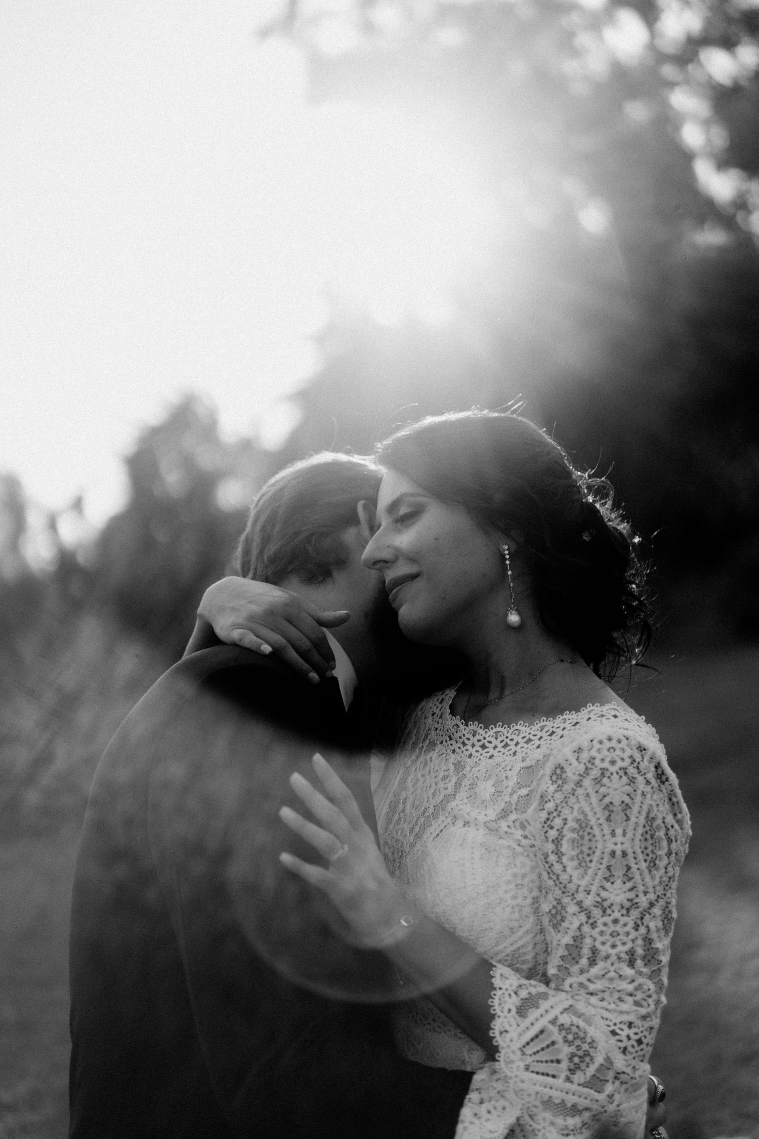 Romantic black and white portrait of a couple embracing outdoors with sunlight creating a dreamy backlit effect.