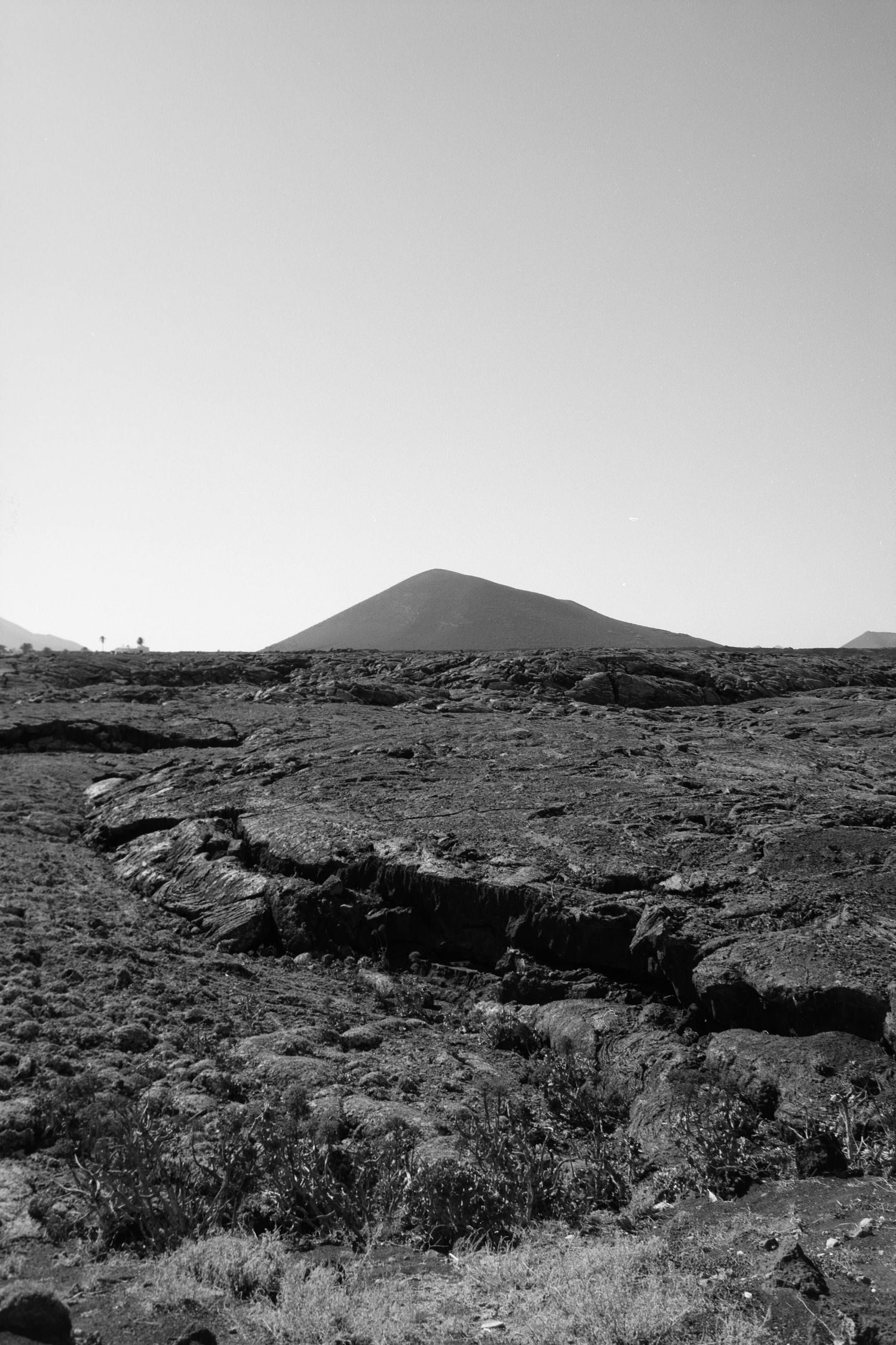 A black and white landscape photo showing a volcanic cone rising above rough, craggy lava fields in a desert terrain.