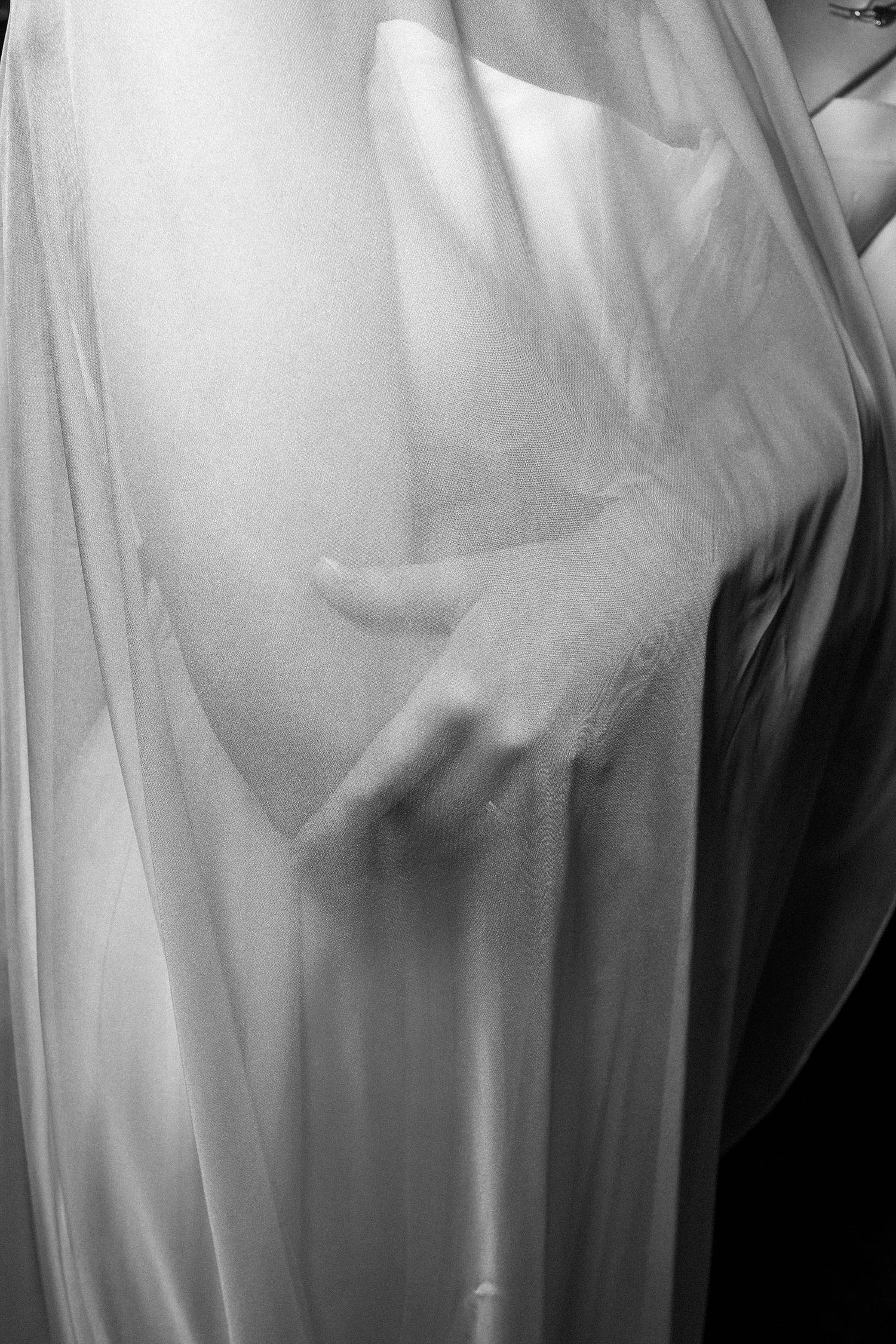 Ethereal black and white photograph showing delicate folds of sheer white fabric with soft shadows creating an abstract pattern.