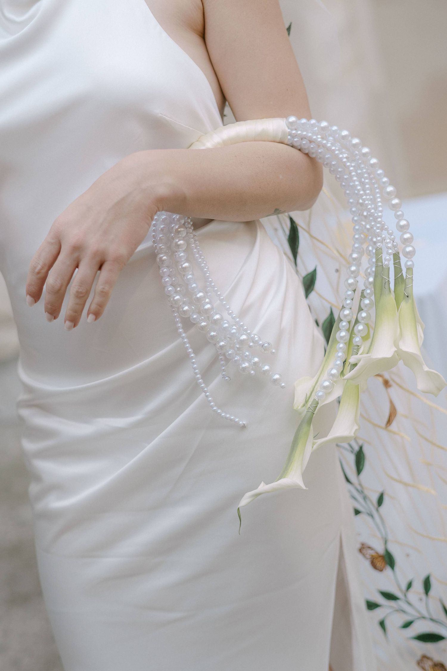 A string of delicate pearl beads drapes elegantly against a flowing white dress with floral embellishments.