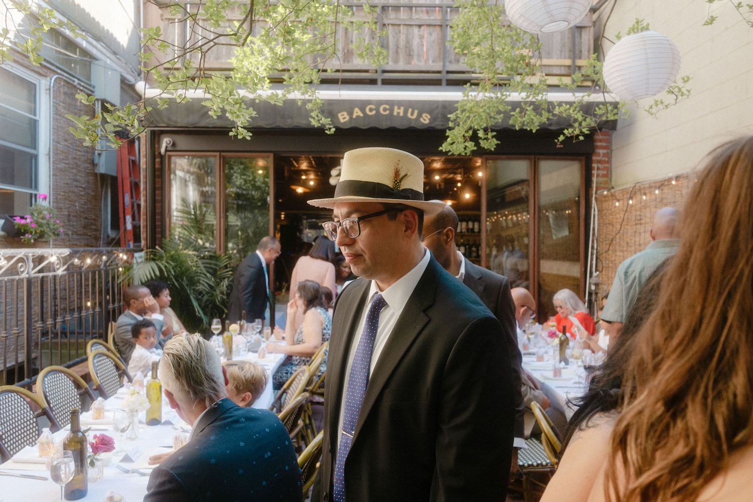Diners enjoy outdoor seating at a charming Parisian cafe with greenery and string lights overhead.