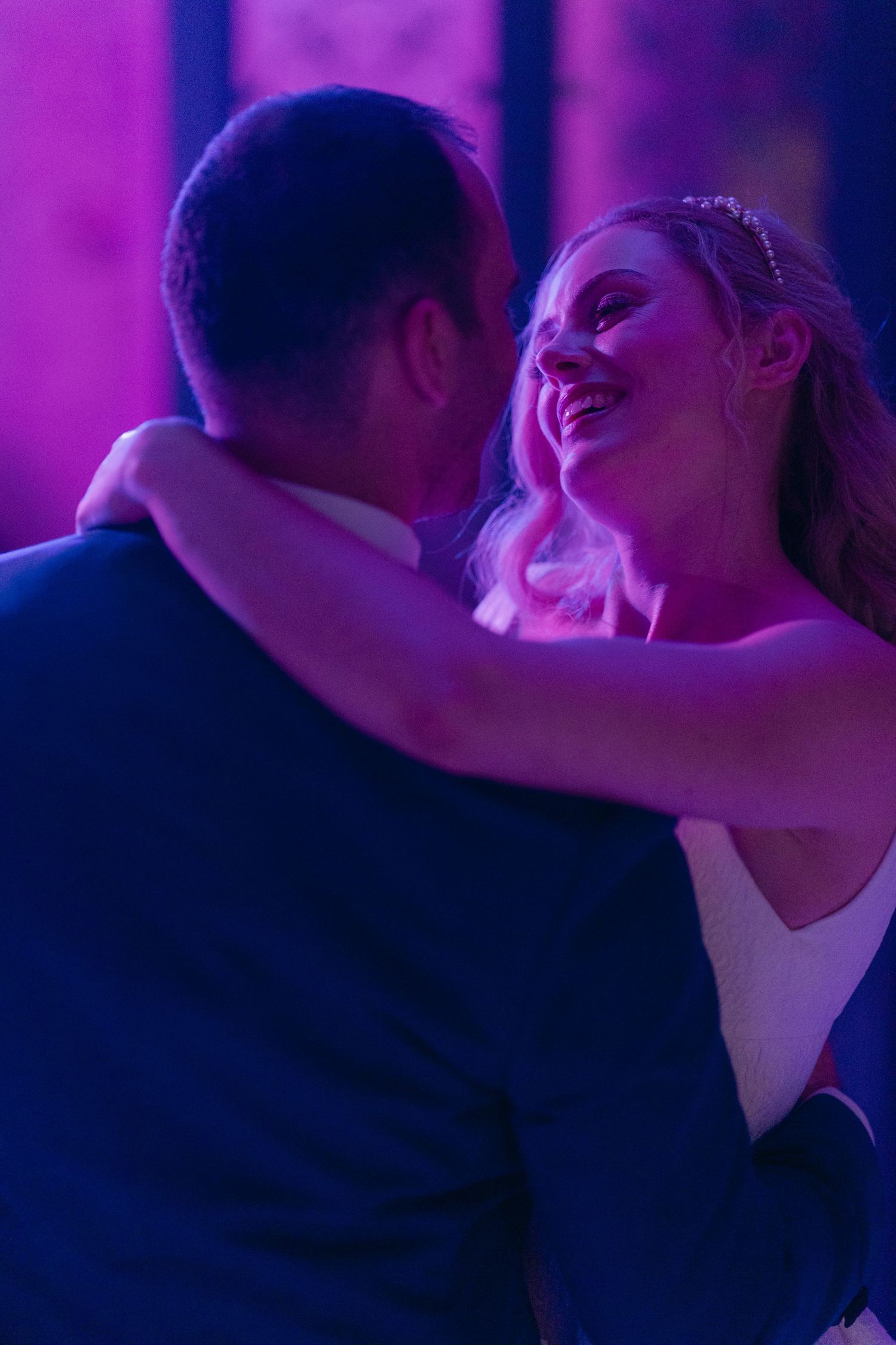 A couple shares a joyful dance moment bathed in purple lighting at what appears to be their wedding reception.